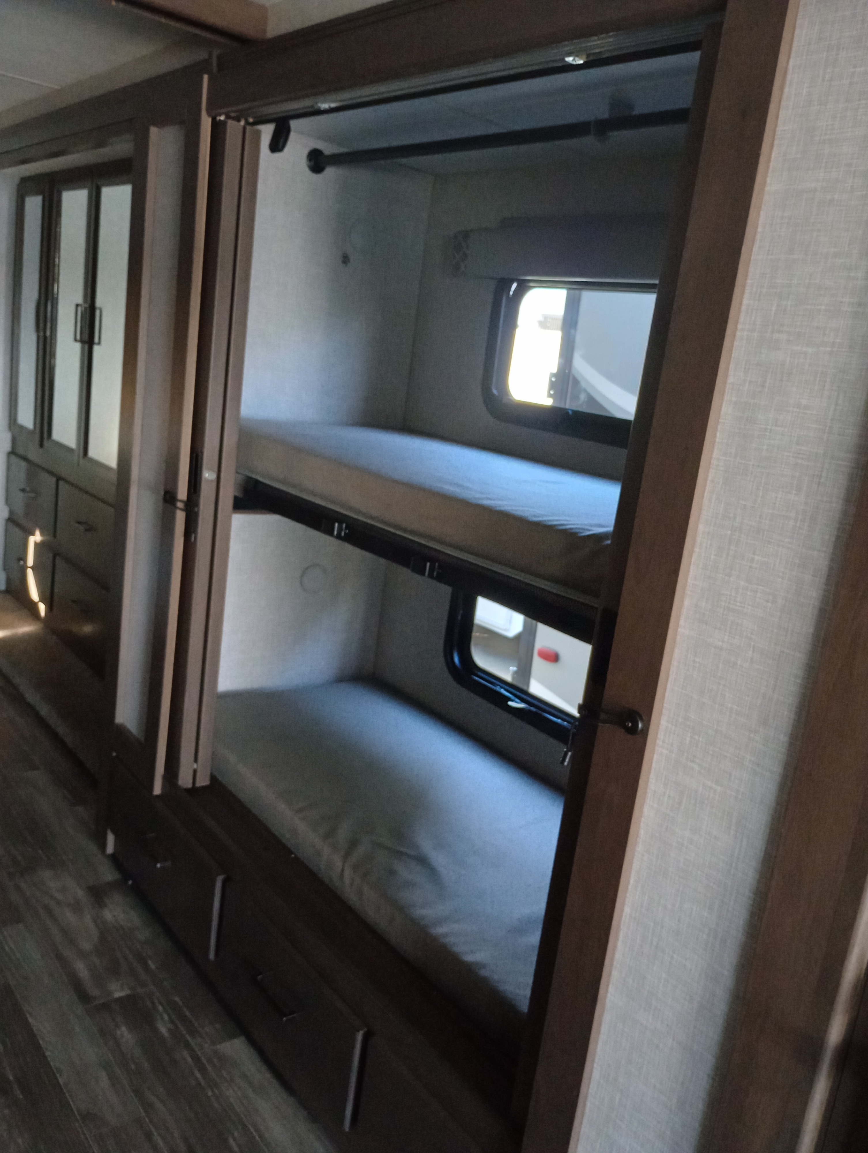 This RV rental interior features compact bunk beds with windows, next to a wardrobe and drawers, for efficient use of space.. Thor Motor Coach Hurricane 2022