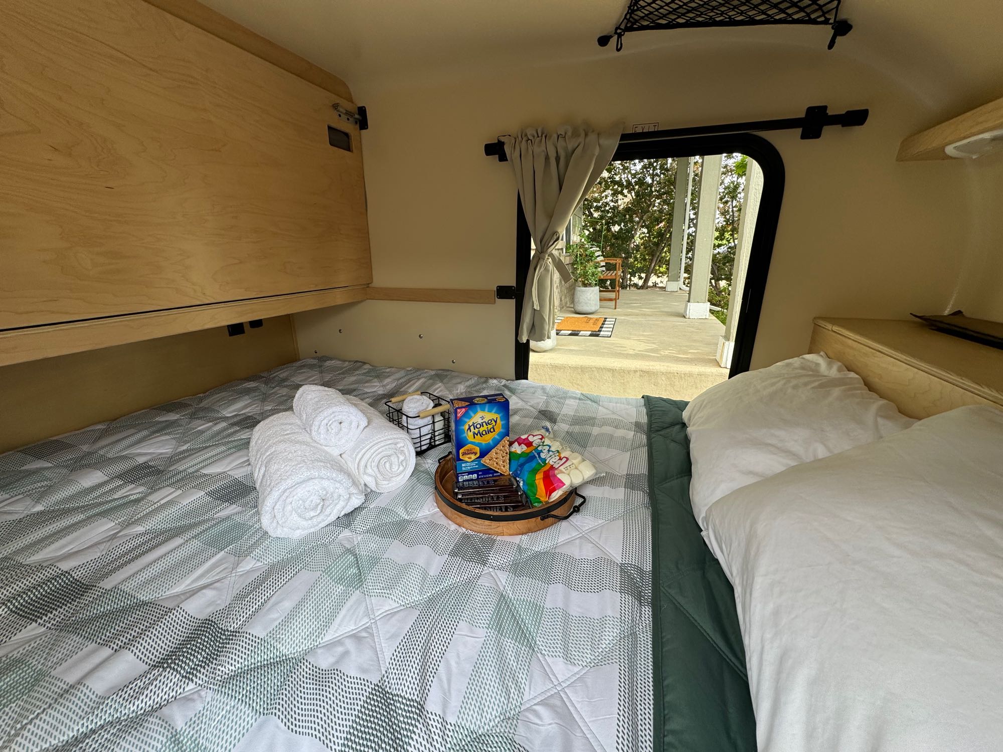 Cozy RV rental interior with a bed, S'mores kit, and an open hatch revealing an outdoor patio. Ready for adventures!. High Altitude Trailers GEN IV XT50 OFF-ROAD TEARDROP 2023