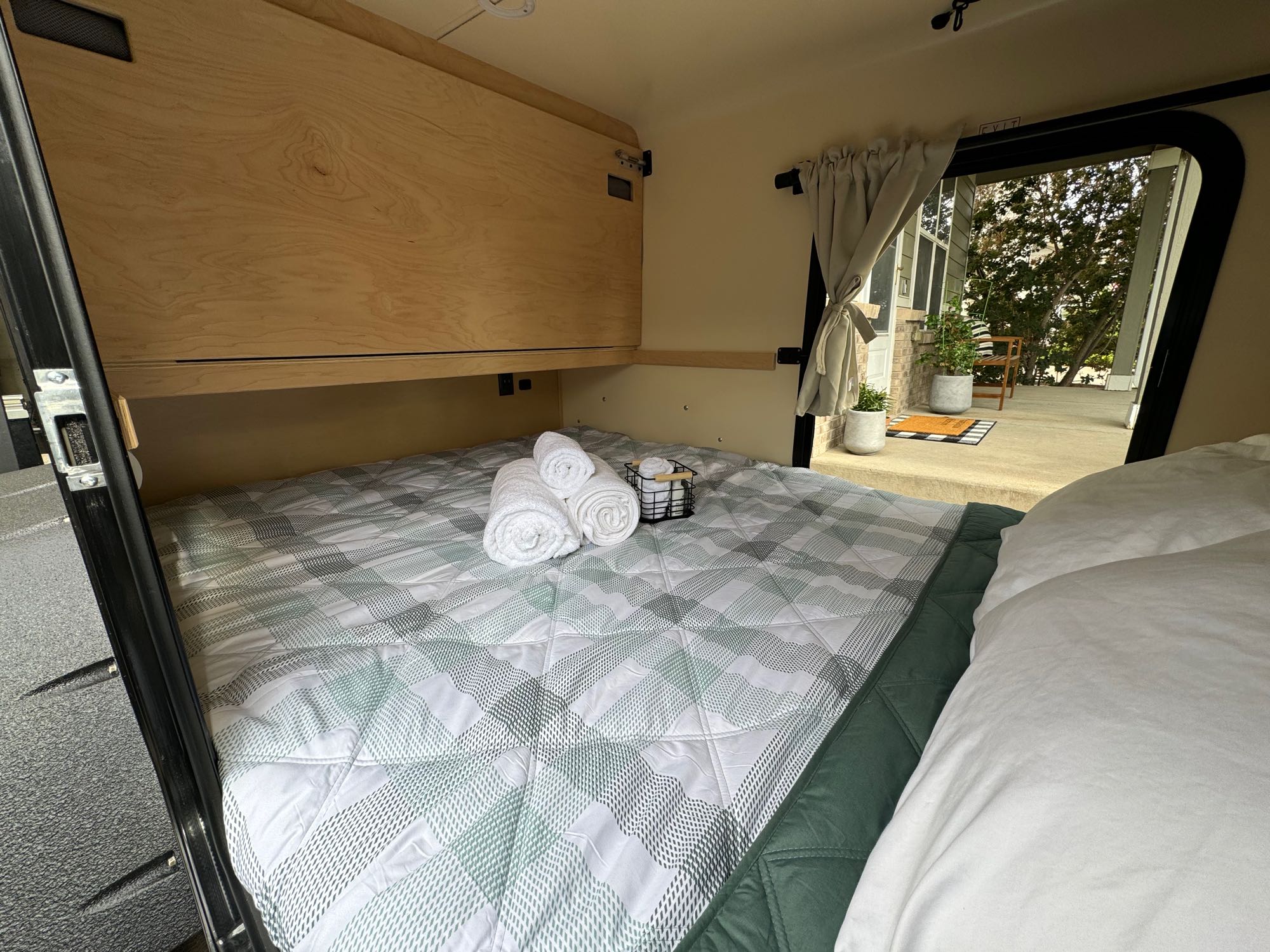 Cozy RV rental interior: A compact bed with plaid bedding, fresh towels, and an open door leading to an inviting patio.. High Altitude Trailers GEN IV XT50 OFF-ROAD TEARDROP 2023