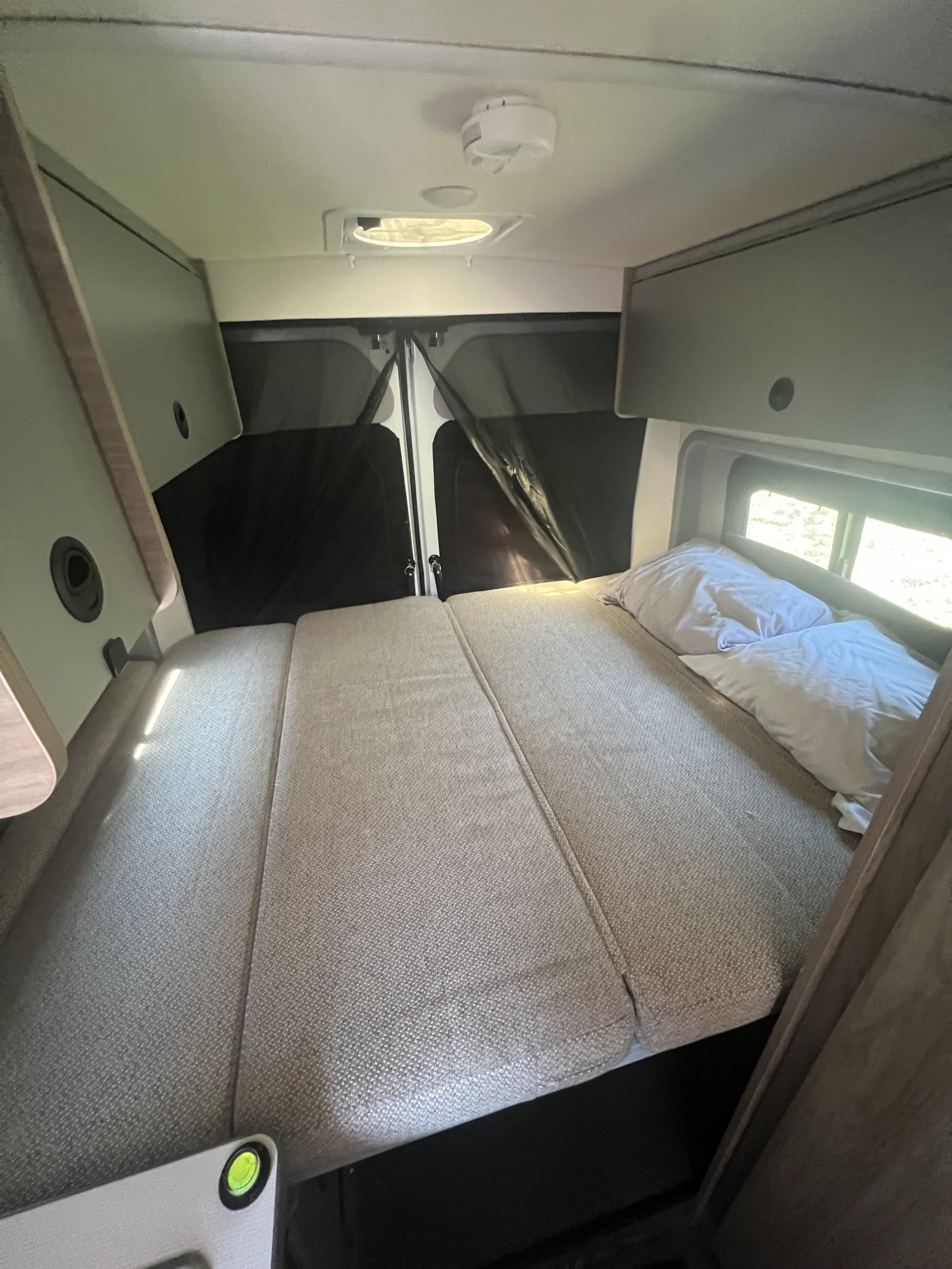 Cozy rv rental interior with a comfortable bed, overhead storage, and rear windows with privacy screens.. Winnebago Solis 59P 2022