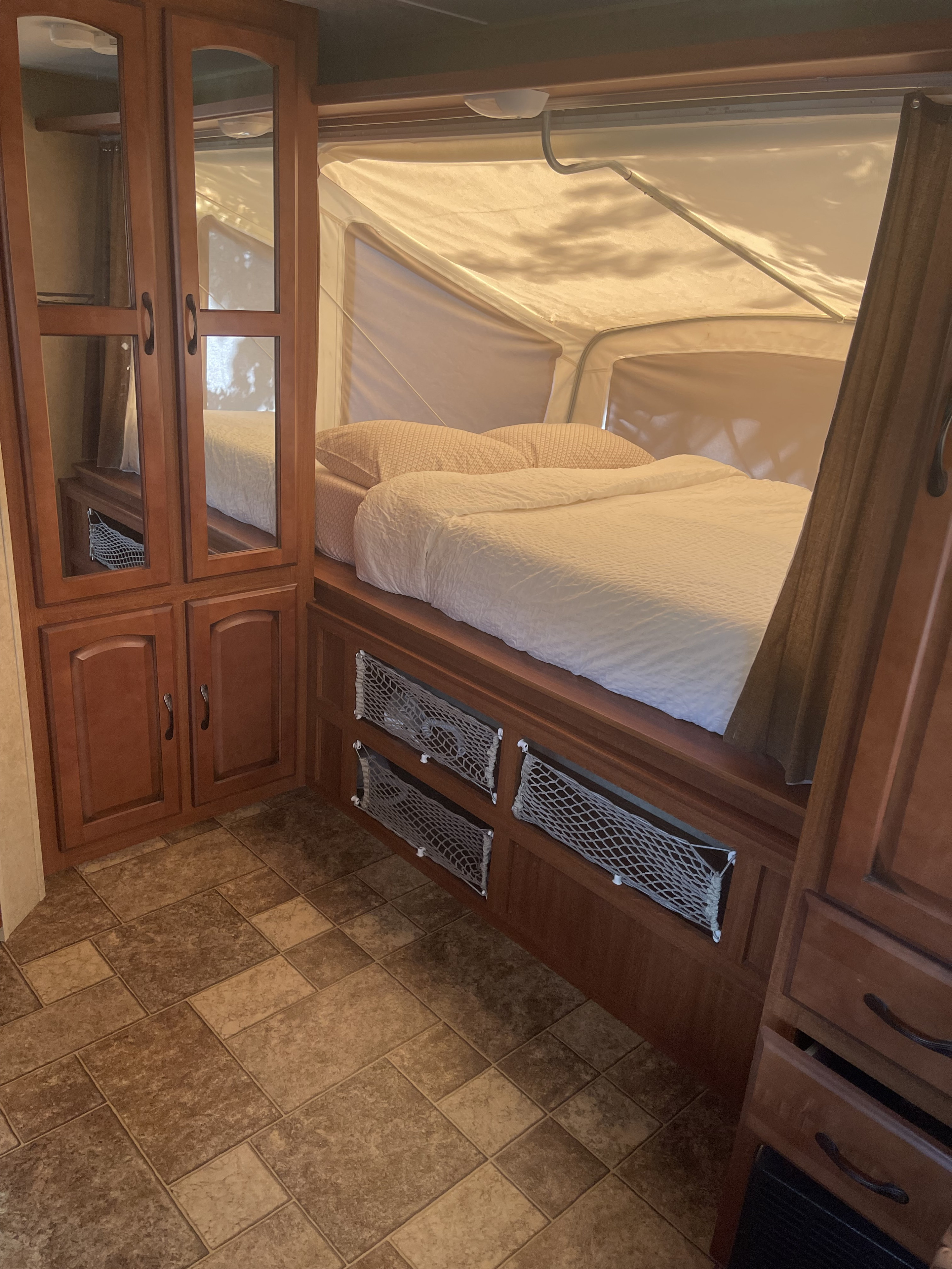 Cozy RV rental sleeping area featuring a pop-up bed, wooden cabinetry, and practical storage nets on a tiled floor.. Forest River Surveyor Sport 2012