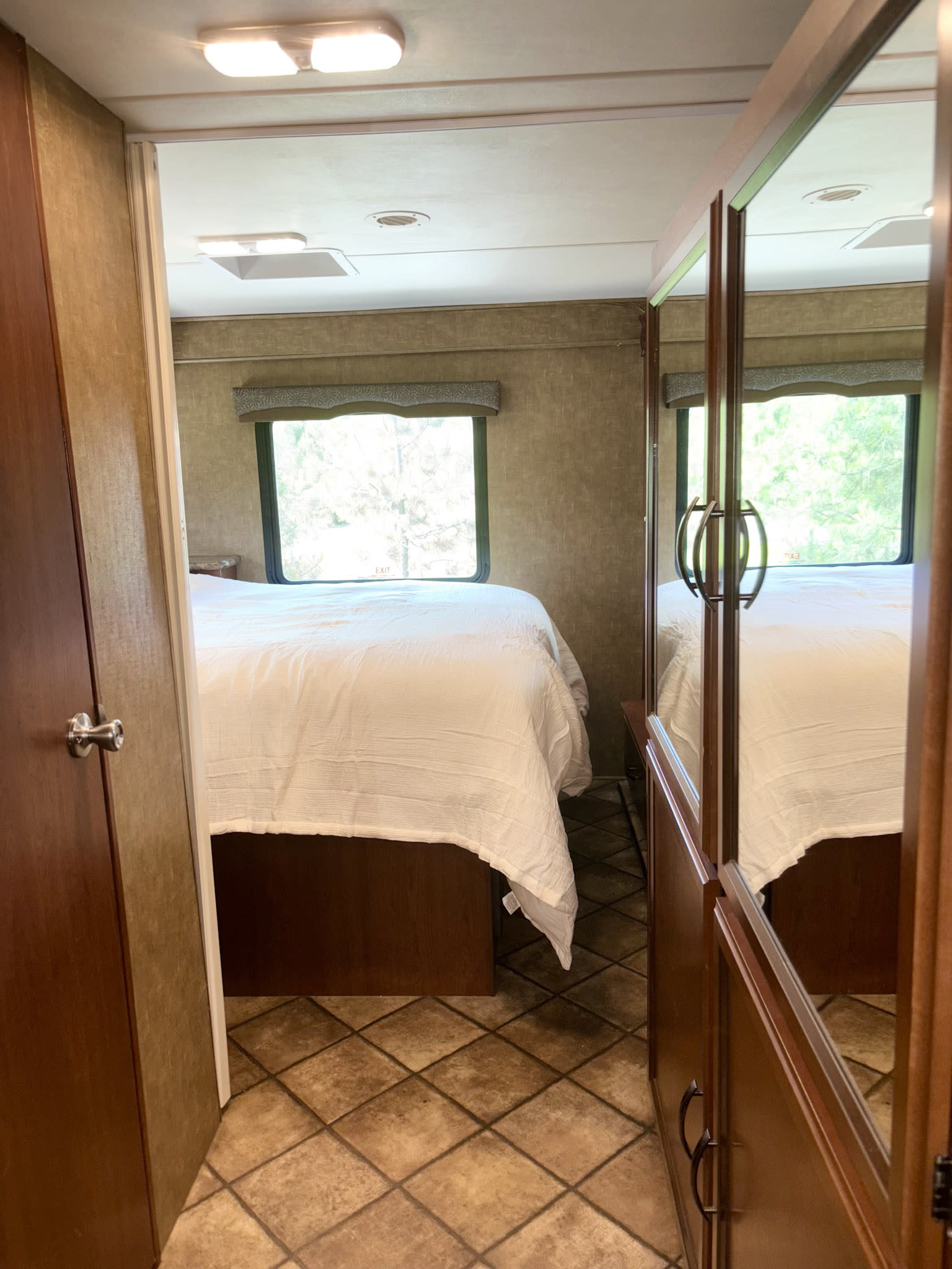 Inside this RV rental, find a comfortable bedroom with a white bed, large window, and mirrored wardrobe.. Thor Chateau 2014