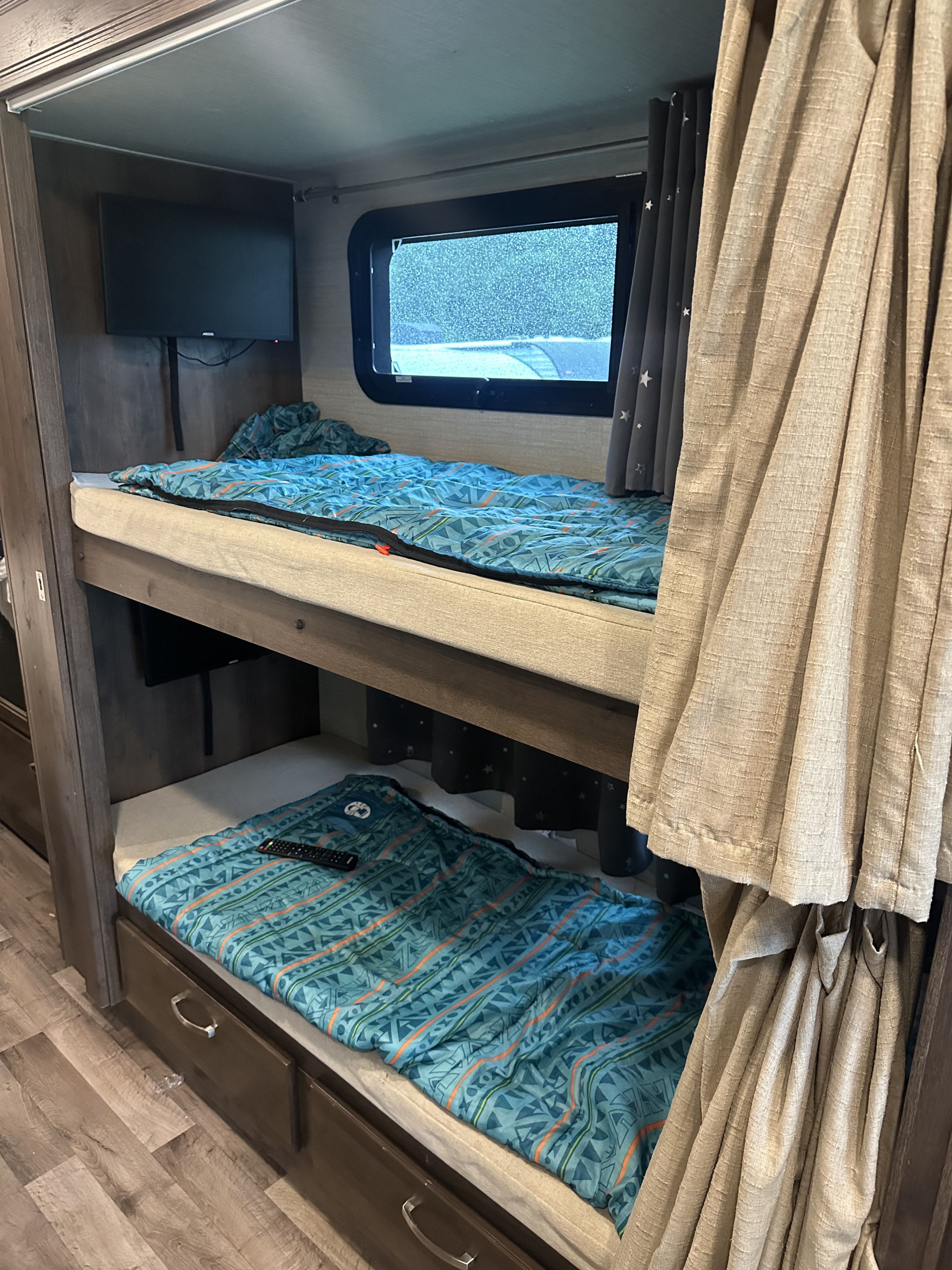 Interior of an RV rental showing two cozy bunk beds with patterned bedding, a wall-mounted TV, and a window.. Jayco Alante 2020