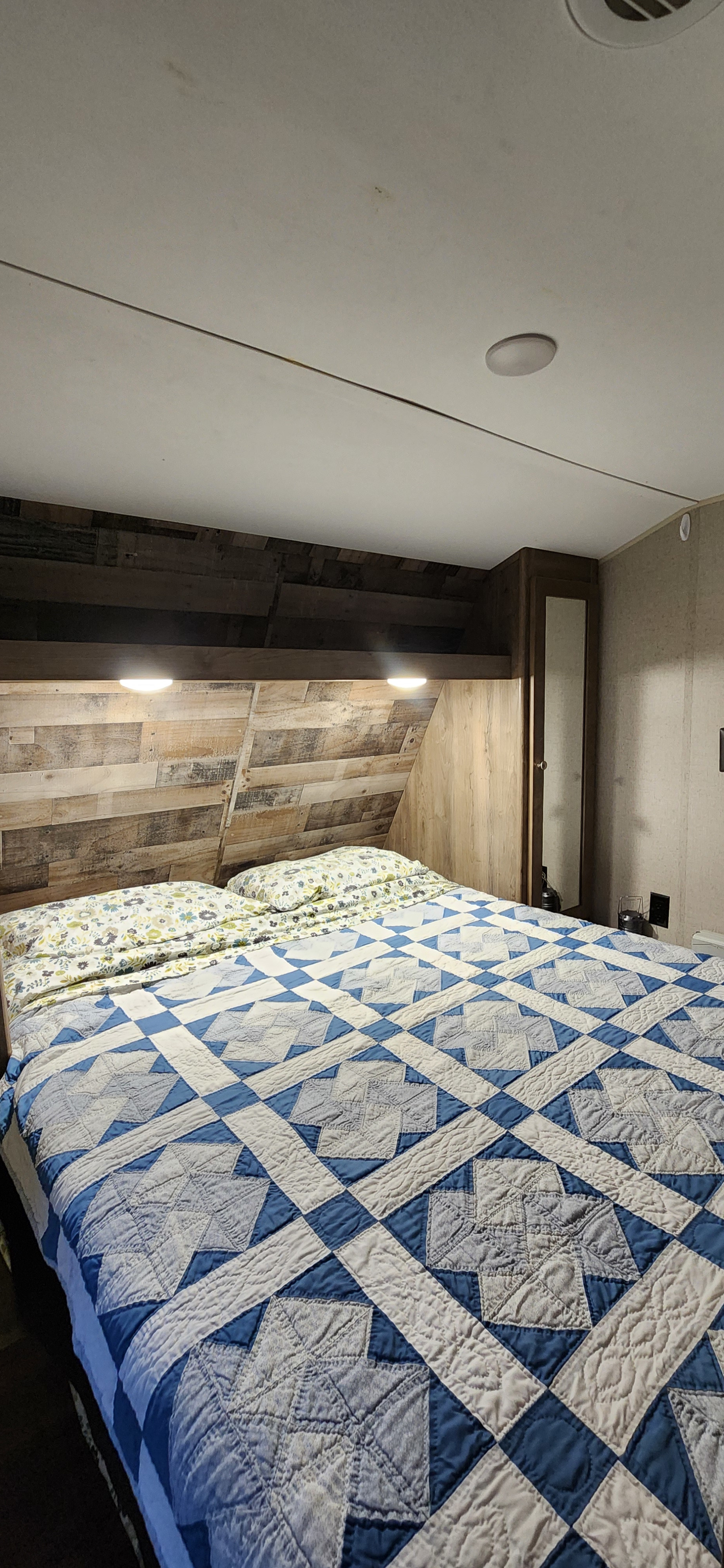 Relax in this RV rental's cozy bedroom. Features a comfortable bed with a blue quilt & wood paneling.. Aspen Trail Aspen Trail Trailer 2019