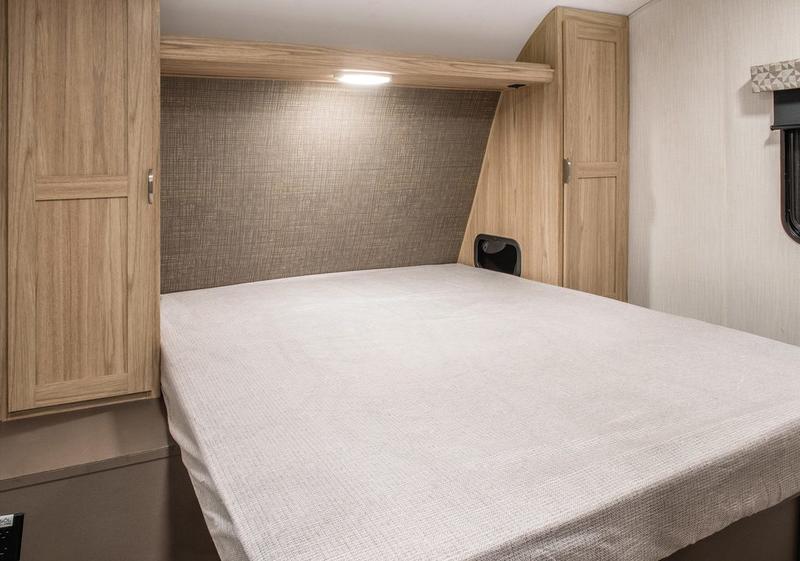 Interior of an RV rental bedroom featuring a full bed, overhead light, and integrated wood cabinets for efficient space.. Cruiser RV Avenir 2024