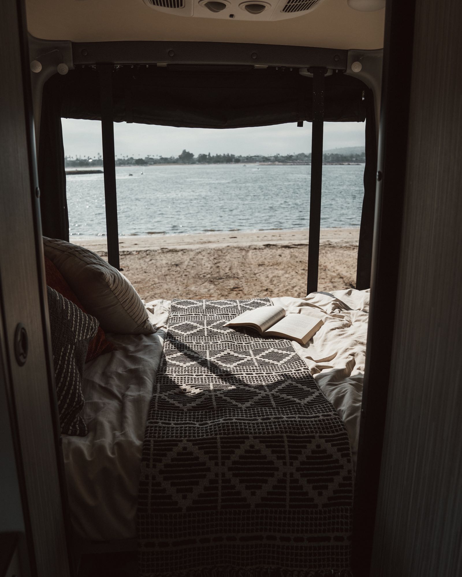 Cozy RV rental bedroom with an open book and stunning beach view, perfect for relaxation and travel.. Winnebago Revel 2022