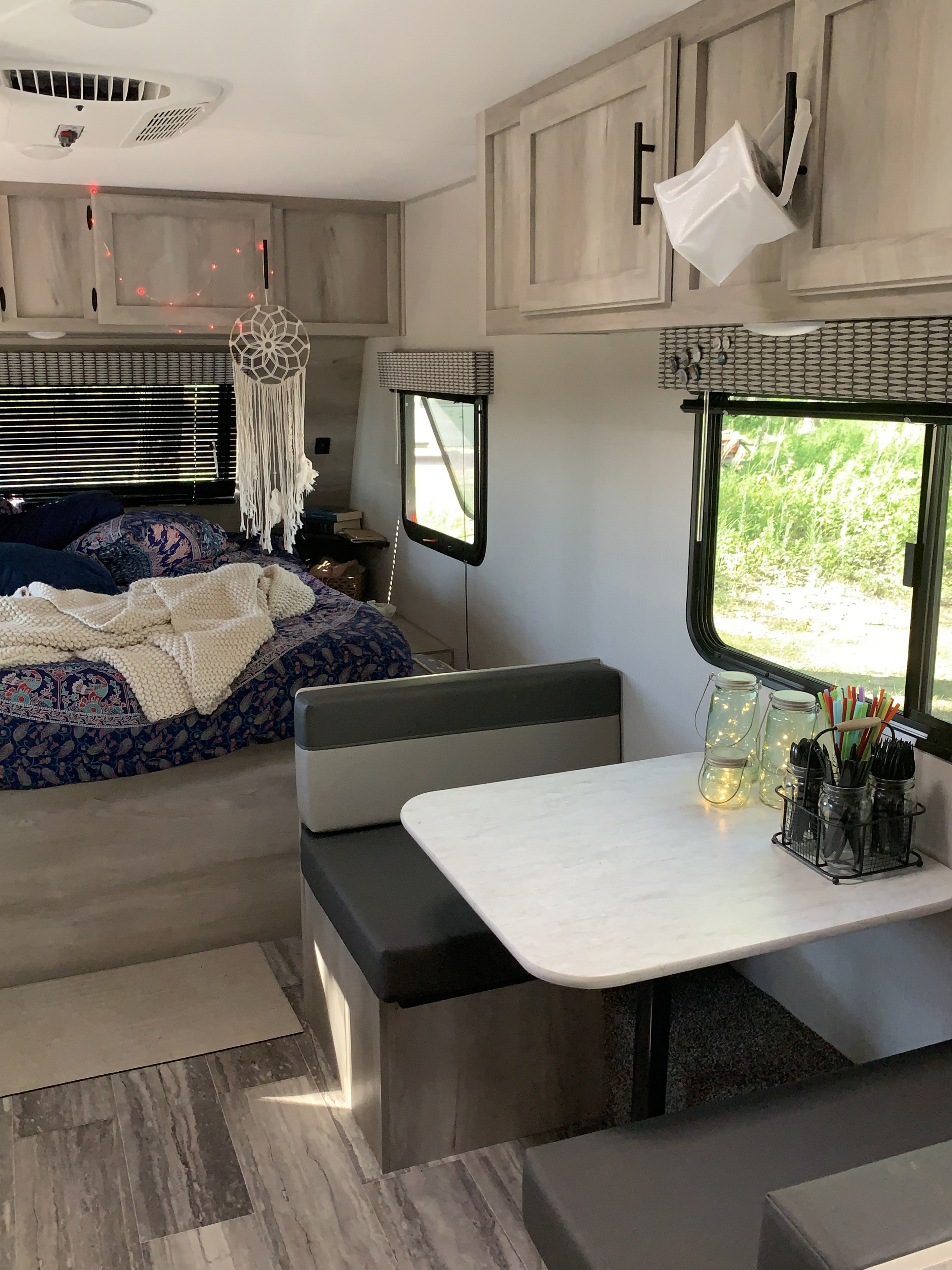 Inside an RV rental: a stylish bedroom with a patterned bedspread and dream catcher, plus a dinette with bench seating.. KZ Sportsmen classic 160QB 2021