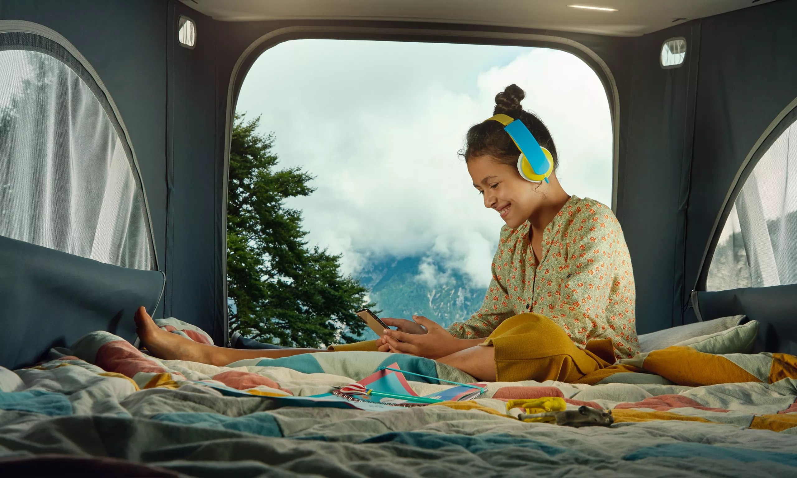 Young girl relaxing in an RV rental, enjoying the scenic mountain view while on her phone. Perfect for travel & camping.. Volkswagen California T6.1 2024