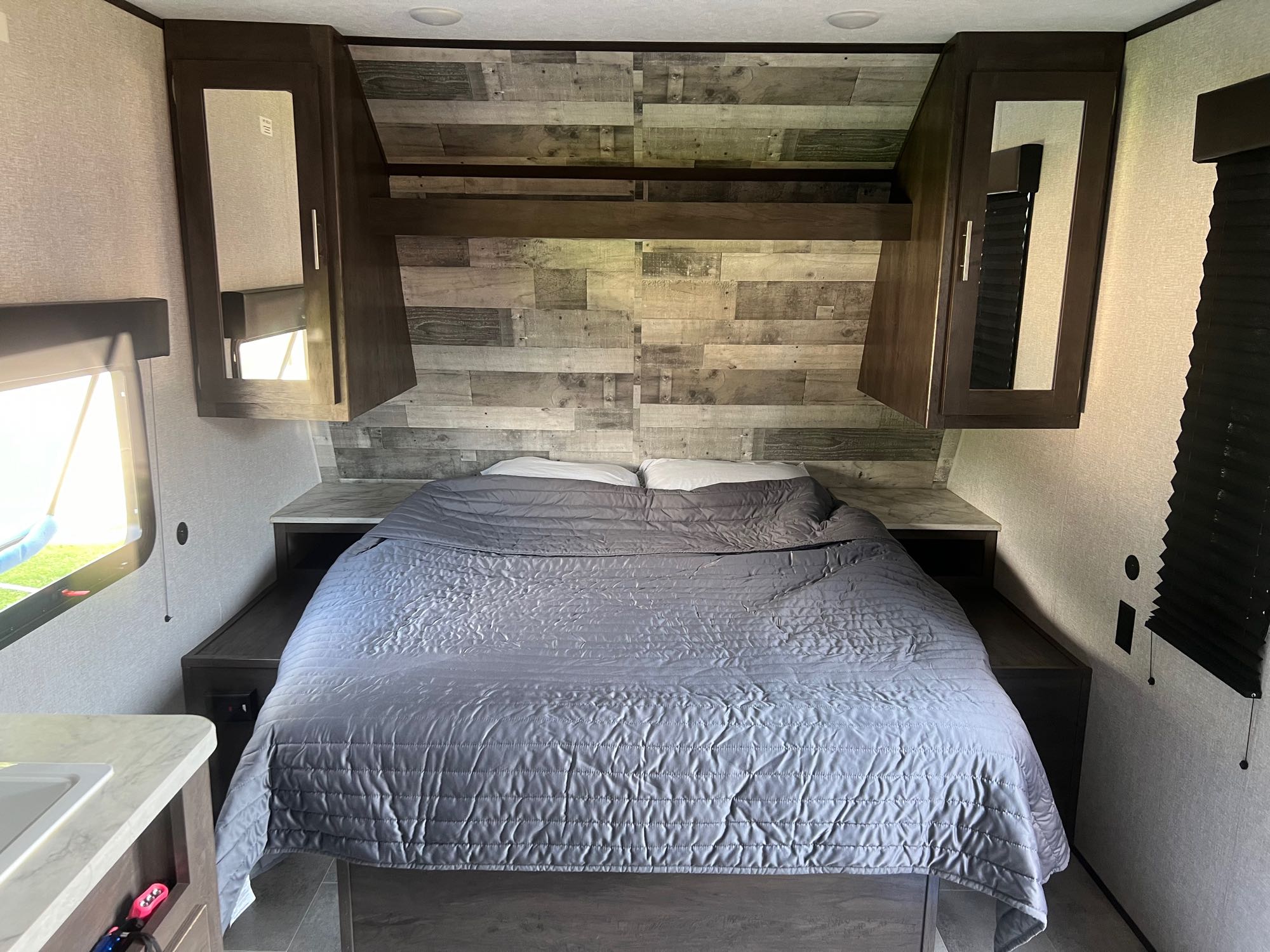 RV rental bedroom: A comfortable grey bed, textured walls, and overhead mirrored cabinets, with a stylish wood-plank headboard.. Dutchmen Coleman Lantern LT 2021