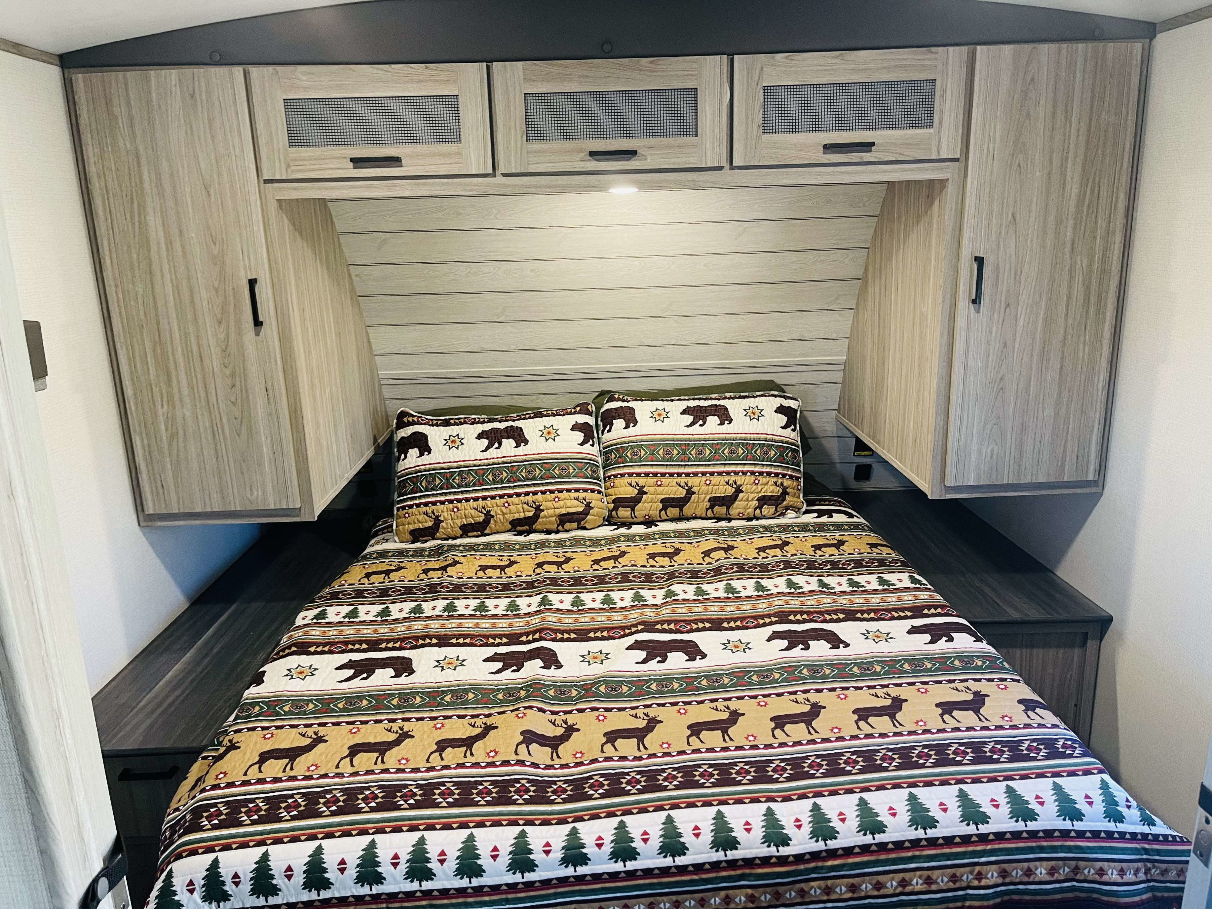 Cozy RV rental bedroom with nature-themed bedding, overhead cabinets, and built-in nightstands.. Keystone RV Passport GT Ultra Lite 2023