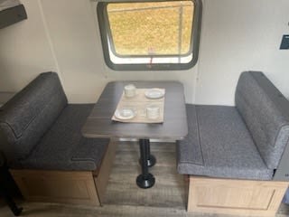 This cozy rv rental dinette features grey benches, a small table with dishes, and a window for scenic views.. Forest River Wolf Den 2024