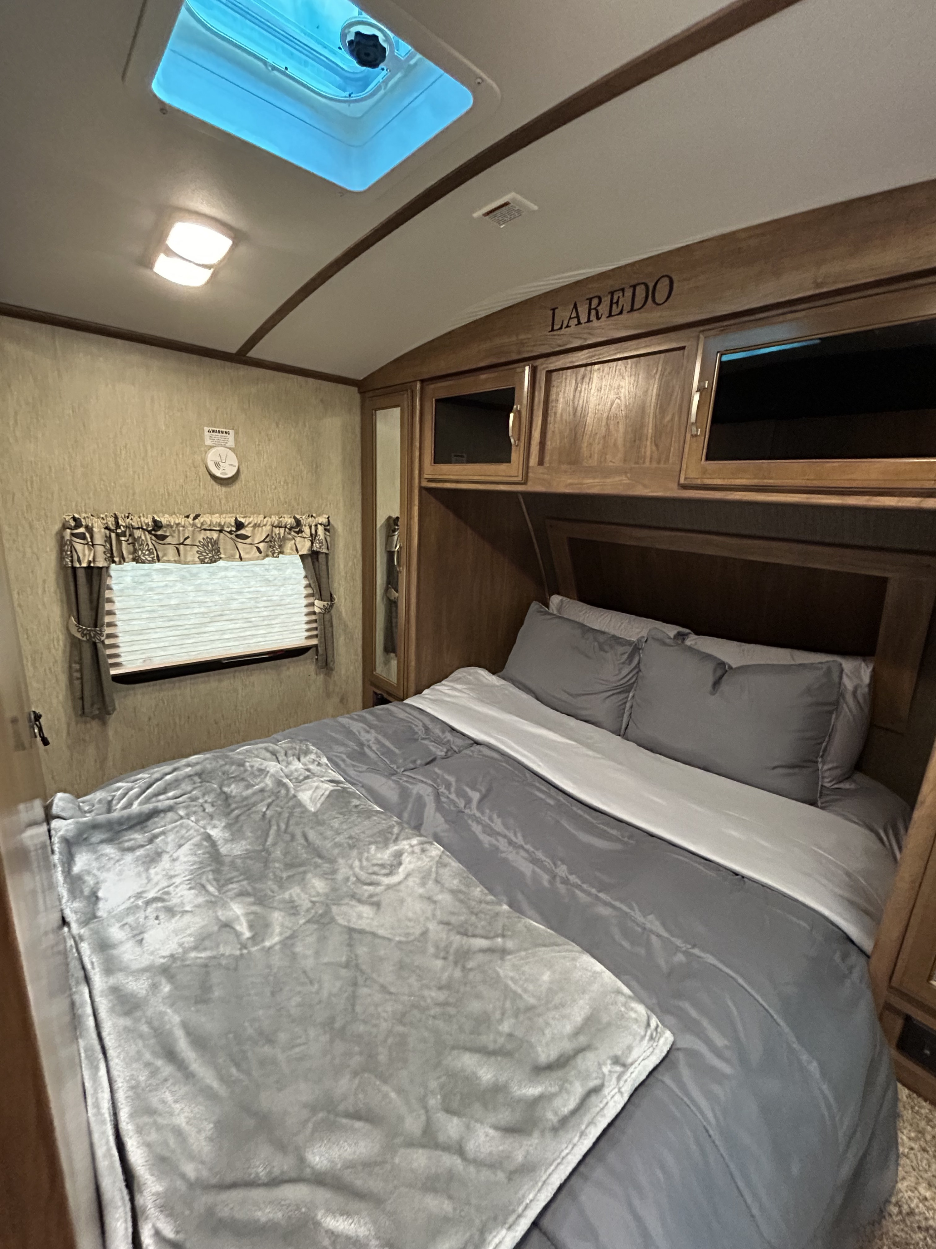 RV rental bedroom featuring a comfy bed with grey linens, ample storage, and a bright skylight. Perfect for your next adventure.. Keystone RV Laredo 2016