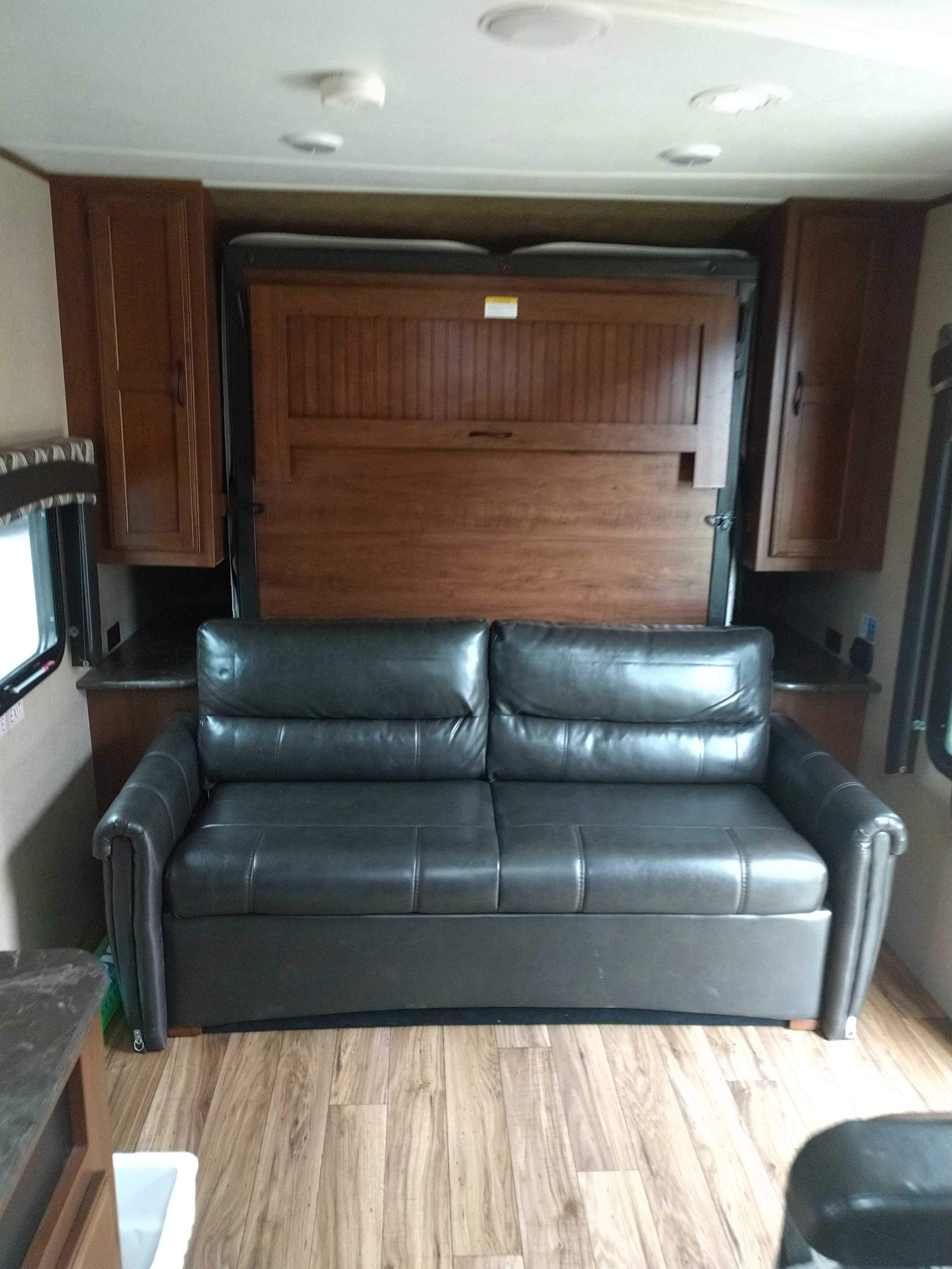 Spacious RV rental interior featuring a dark leather pull-out sofa, a hidden murphy bed, and wood storage cabinets.. Jayco 23MB 2016