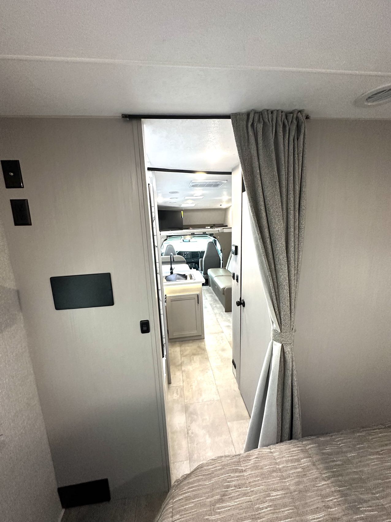 View inside an RV rental. From the bedroom, a doorway leads to the kitchen and cockpit area, with a gray curtain tied back.. Forest River Coachmen FreeLander 27QB 2025