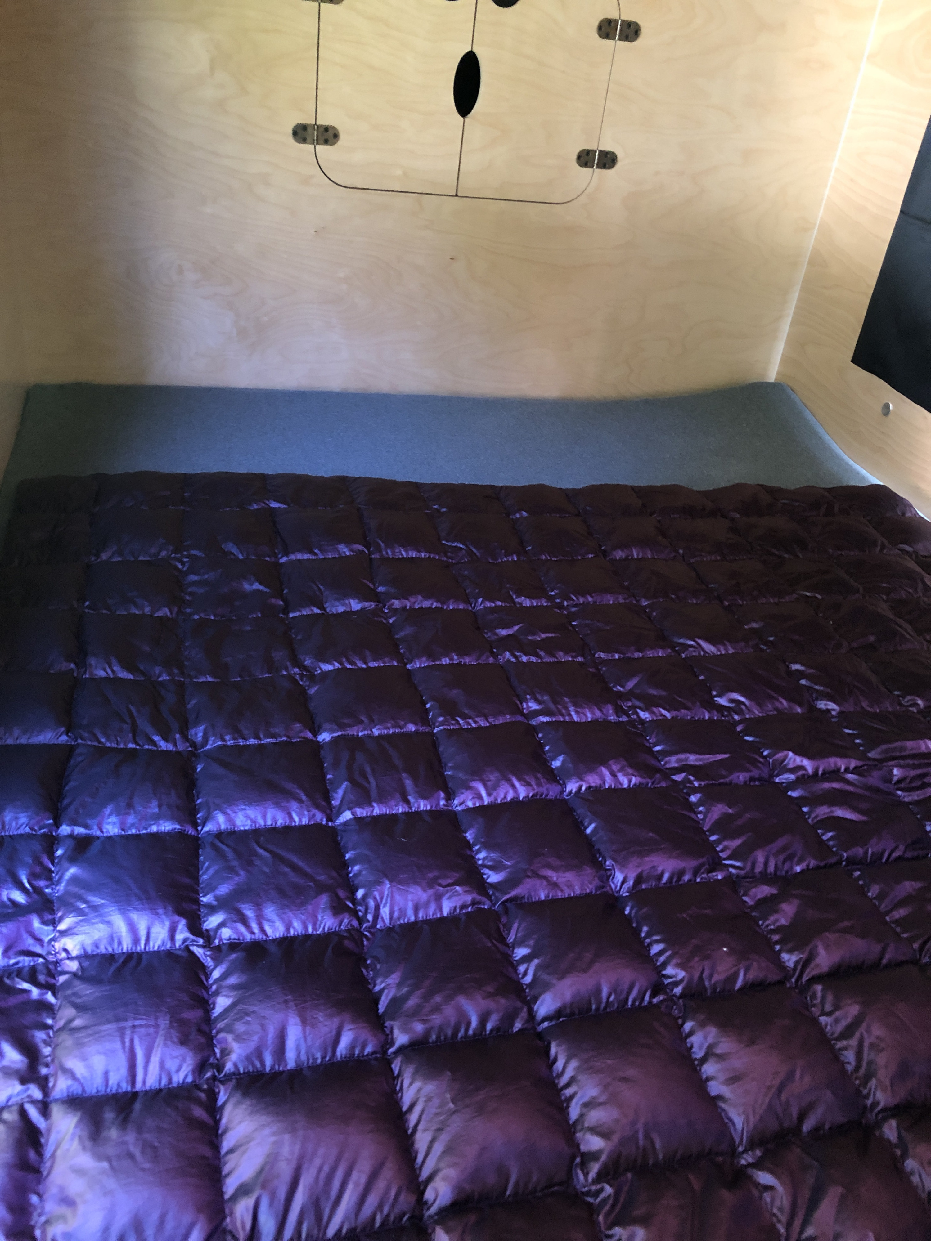 Inside a cozy RV rental: a plush purple quilted blanket on a bed, set against light wood walls with a minimalist design.. Hiker 5X9 MR 2023