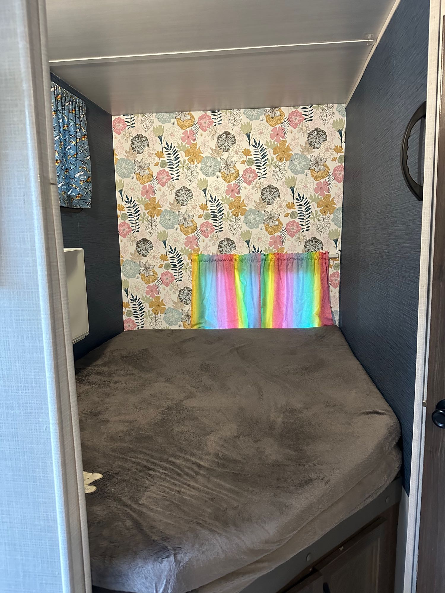 Cozy RV rental bunk bed featuring vibrant floral wallpaper, a rainbow curtain, and a comfy brown mattress.. Winnebago Voyage 2021