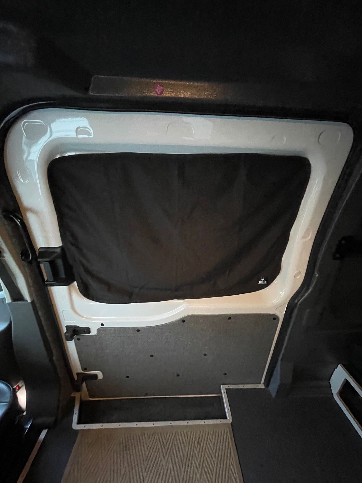 RV rental interior: black window cover on rear door for privacy, with white trim and carpeted floor. AXIS logo visible.. Ford Transit 2021