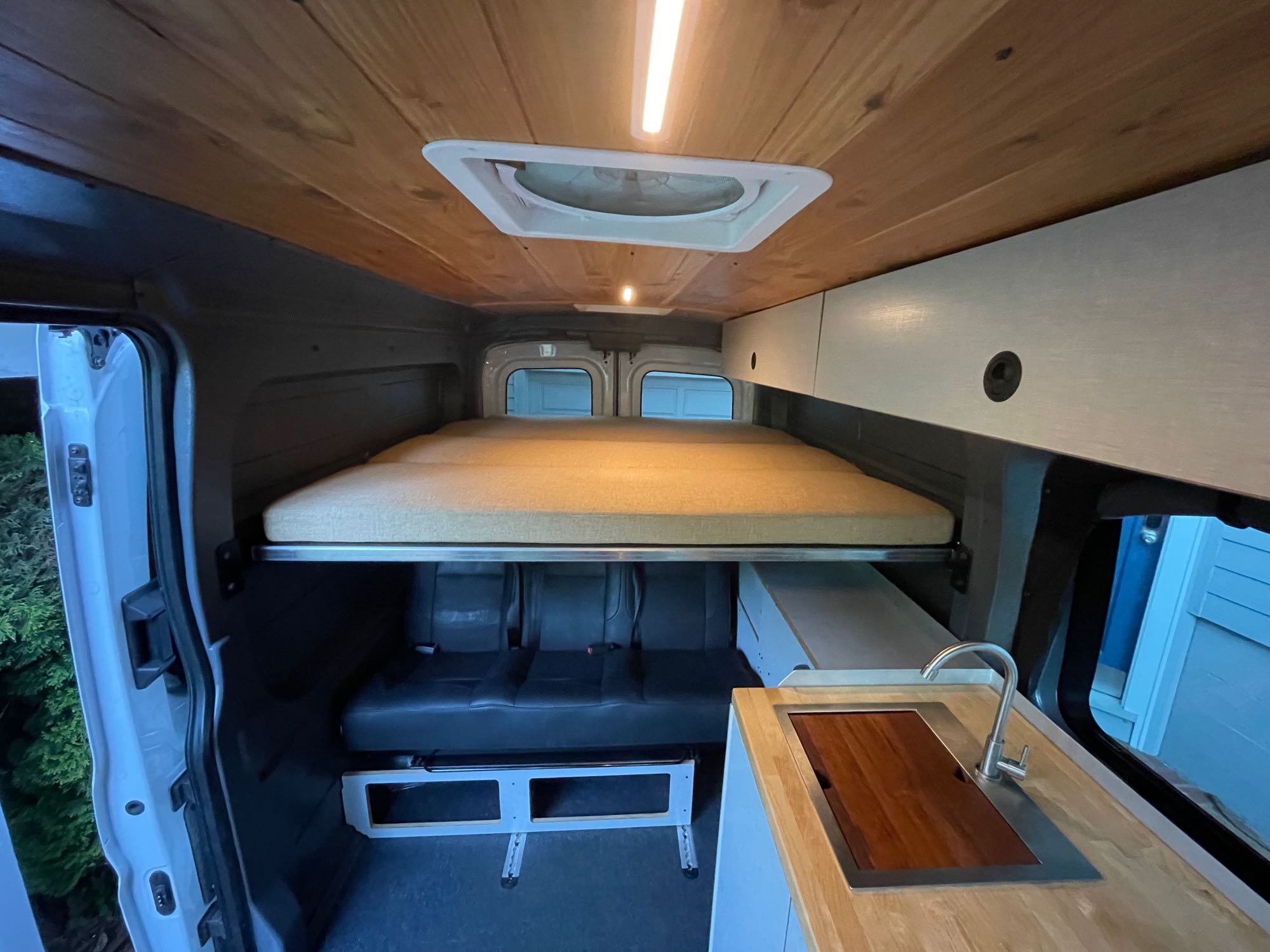 Inside a modern RV rental camper van with an elevated bed, convertible seating, and a compact kitchen counter with sink.. Ford Transit 2021