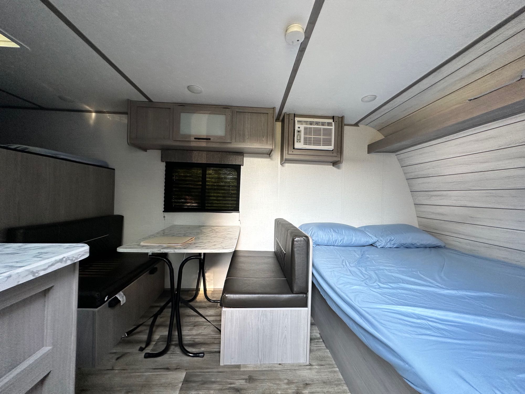 Cozy RV rental interior featuring a dinette, comfortable bed, overhead storage, and AC unit for compact travel.. Coleman Lantern 17b 2024
