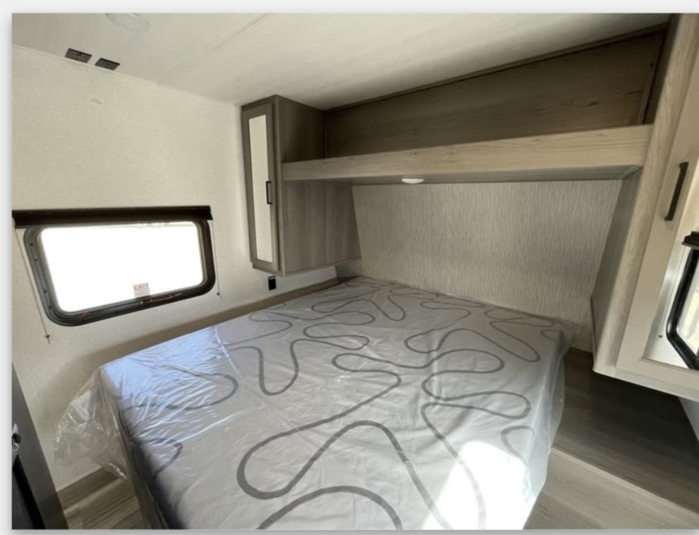 RV rental bedroom: a cozy space with a plastic-covered bed, window, and overhead storage for your travels.. Keystone RV Hideout Sport 2024
