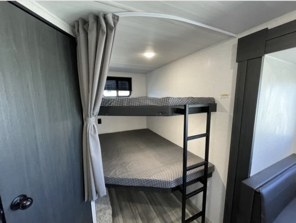 RV rental featuring two bunk beds with ladder and privacy curtain. Ideal sleeping for family campers, ensuring comfort and space.. Keystone RV Hideout Sport 2024