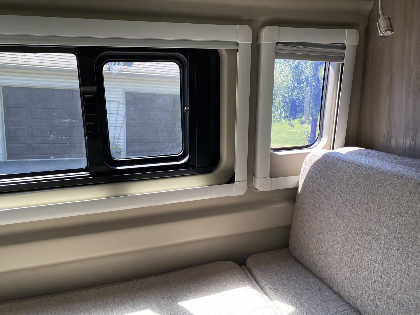 Inside an RV rental, showing comfortable seating and two large windows looking out to a garage and nature.. Thor Tellaro 2021