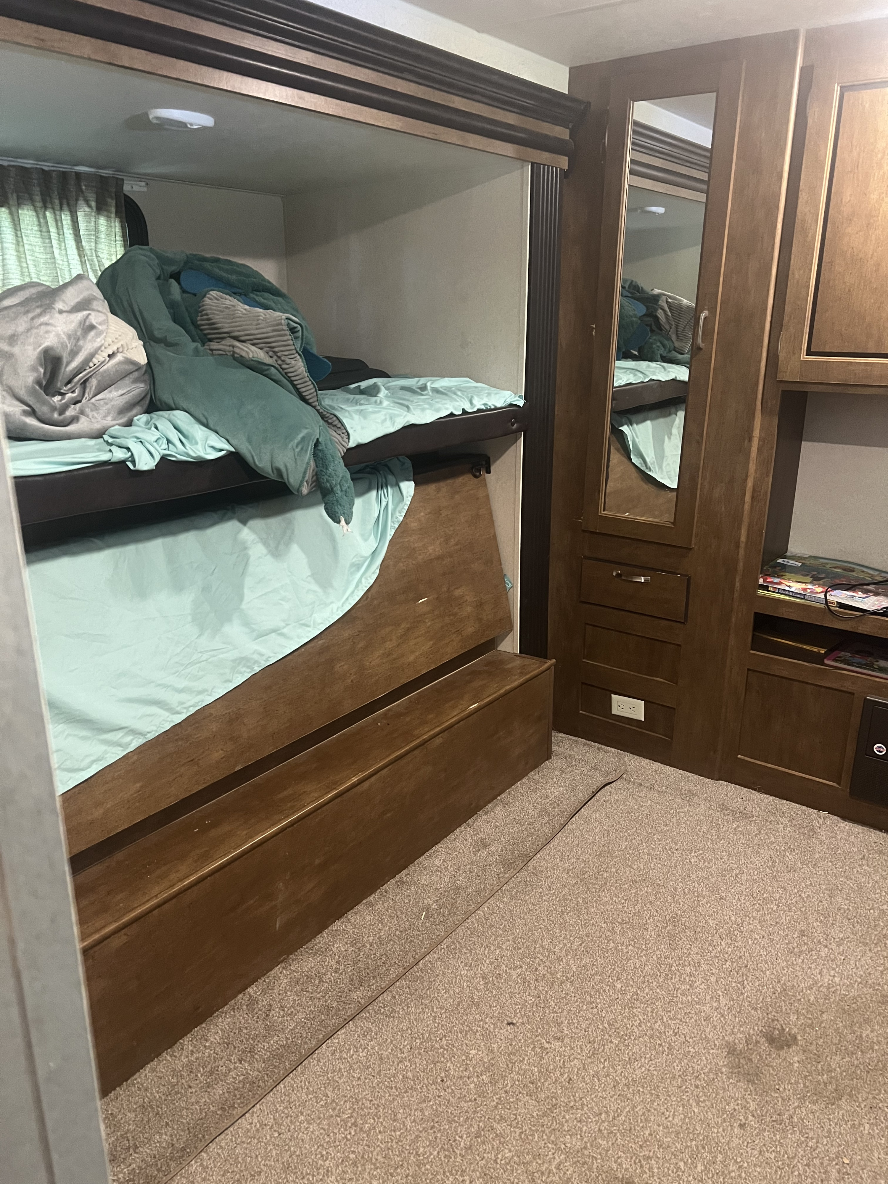 Spacious RV rental interior featuring a cozy lower bunk bed with mint bedding, mirrored wardrobe, and carpeted floor.. Forest River Wildwood 2018