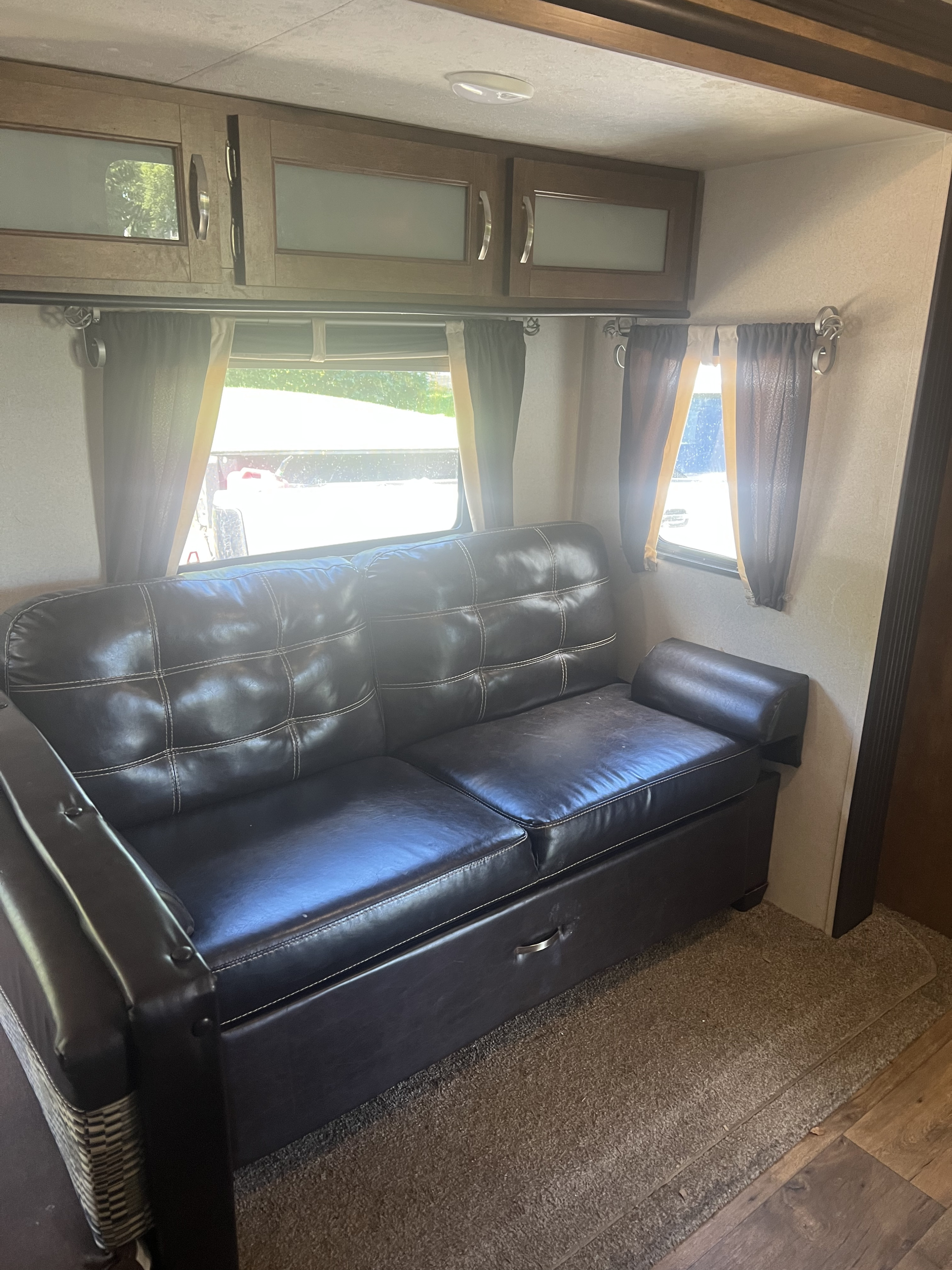 Spacious RV rental interior featuring a dark leather sofa, overhead storage cabinets, and bright side windows.. Forest River Wildwood 2018