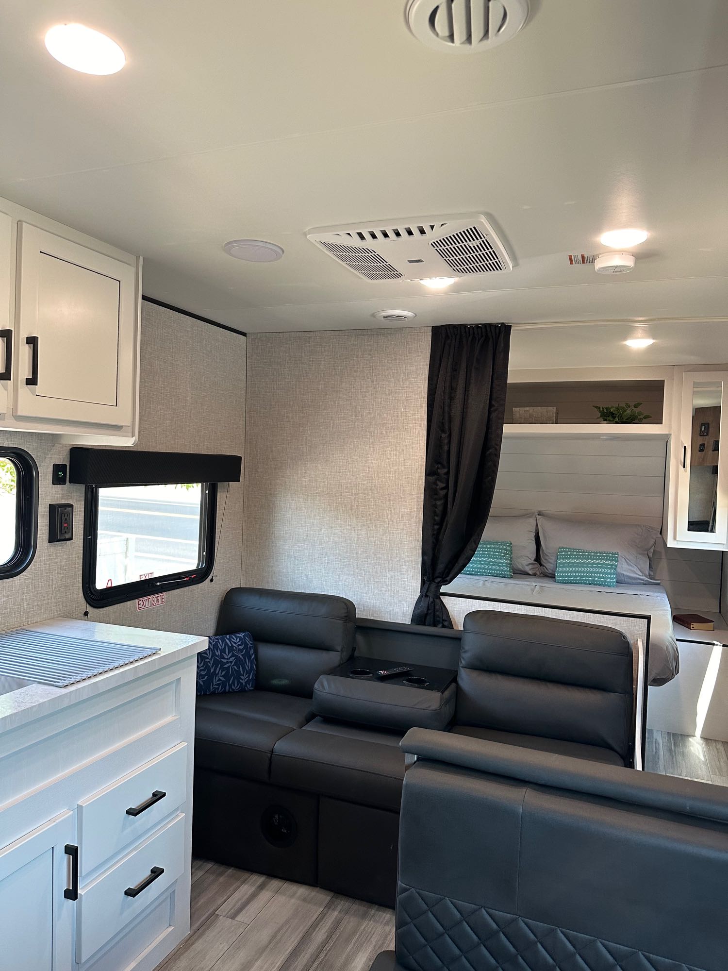 Bright, modern RV rental interior: recliners in the living area, compact kitchen counter, and a curtained bedroom.. Jayco Jay Flight SLX 2024