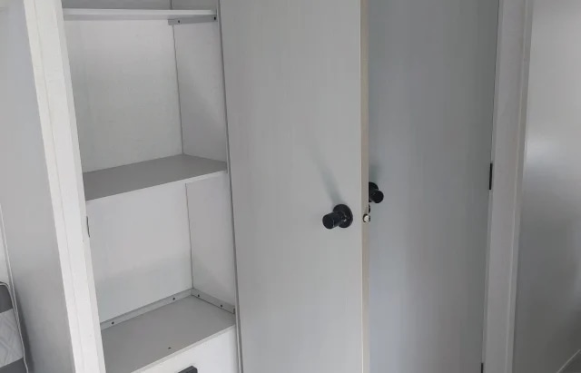Compact storage in an RV rental: A white interior closet with shelves on the left, next to two closed white doors with black handles.. Forest River Salem 2021