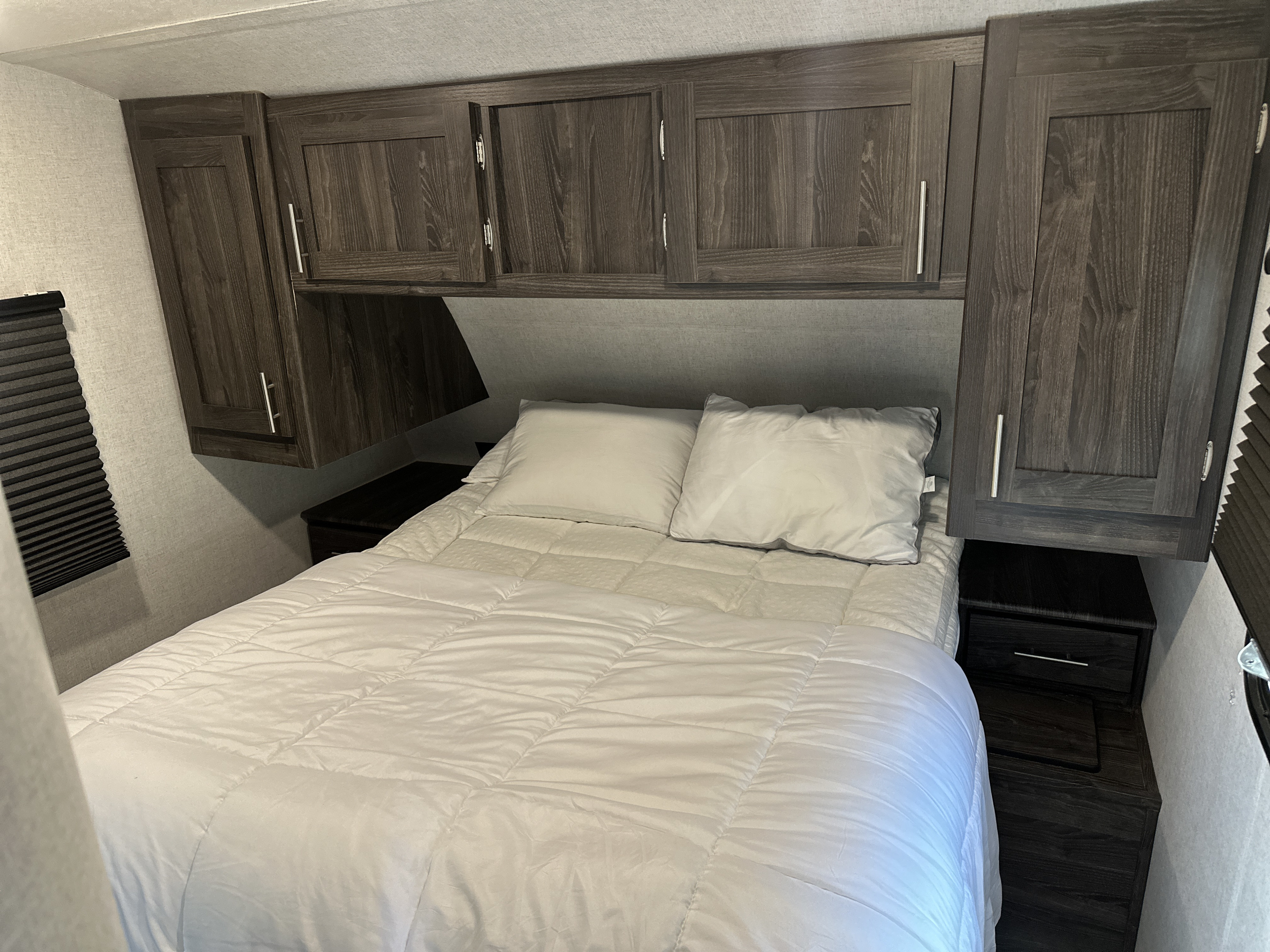 This RV rental bedroom offers a comfortable bed, overhead cabinets, and built-in storage on both sides.. Highland Ridge RV Mesa Ridge Lite 2019