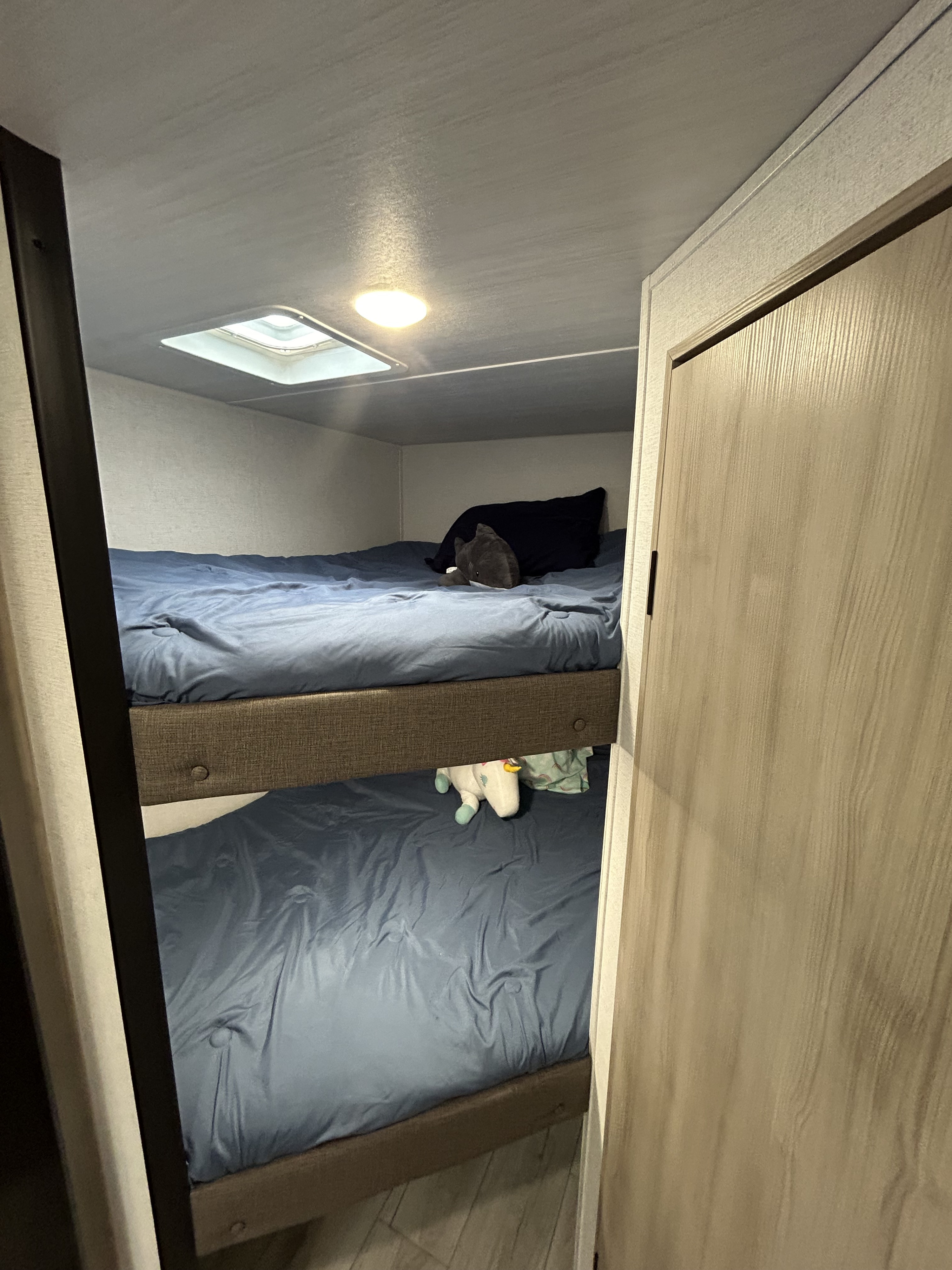Cozy RV rental bunk beds with blue bedding, featuring shark and unicorn plush toys in a compact sleeping area.. East to West Silver Lake 2024