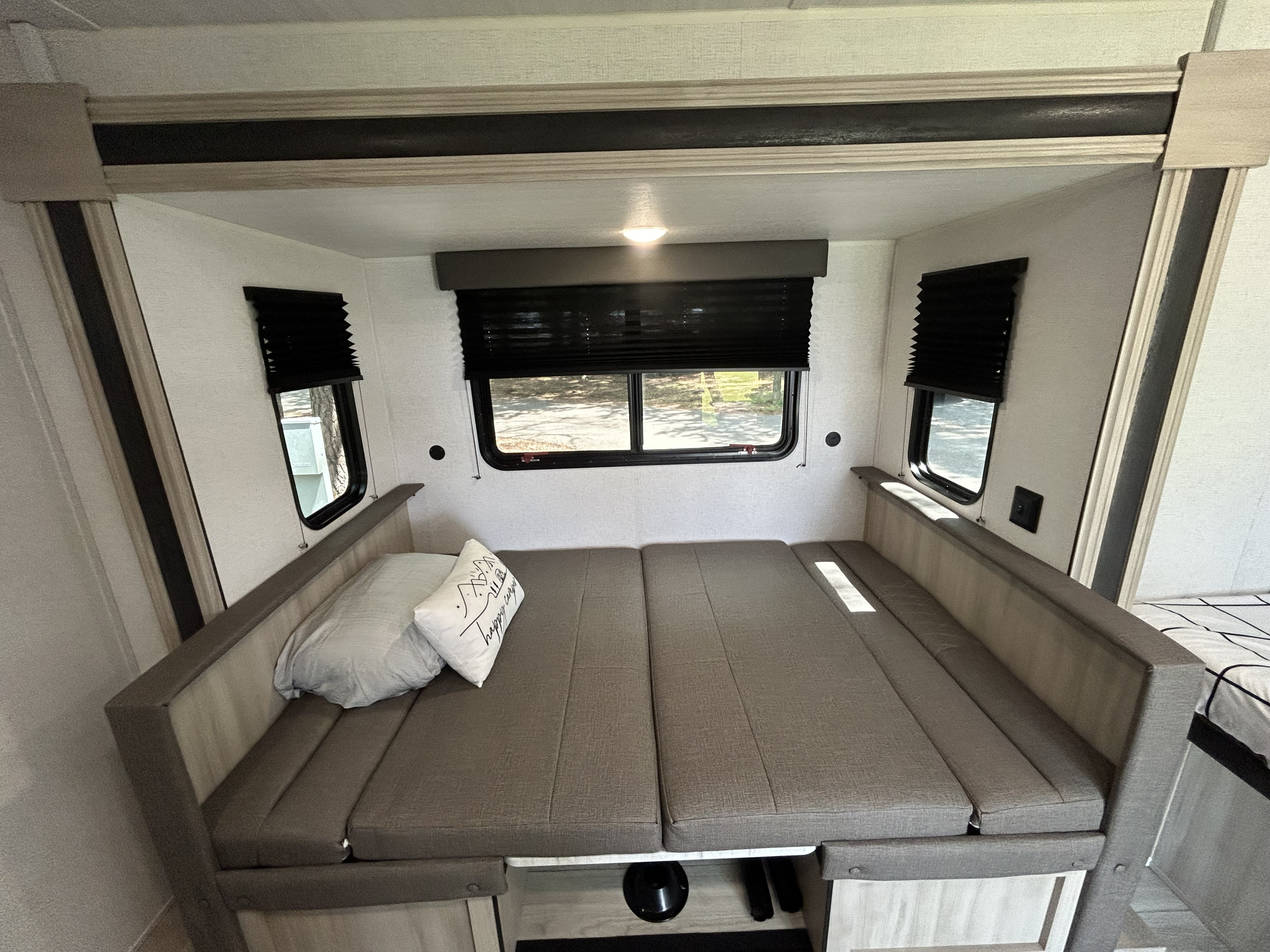 Inside an RV rental: a flexible dinette converts to a comfortable bed, flanked by windows with privacy blinds.. East to West Silver Lake 2024