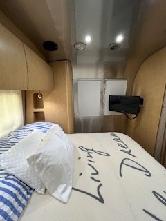 Experience comfort in this **RV rental** bedroom, featuring a comfy bed, mounted TV, and sleek interior for your travel adventures.. Airstream Flying Cloud 2016