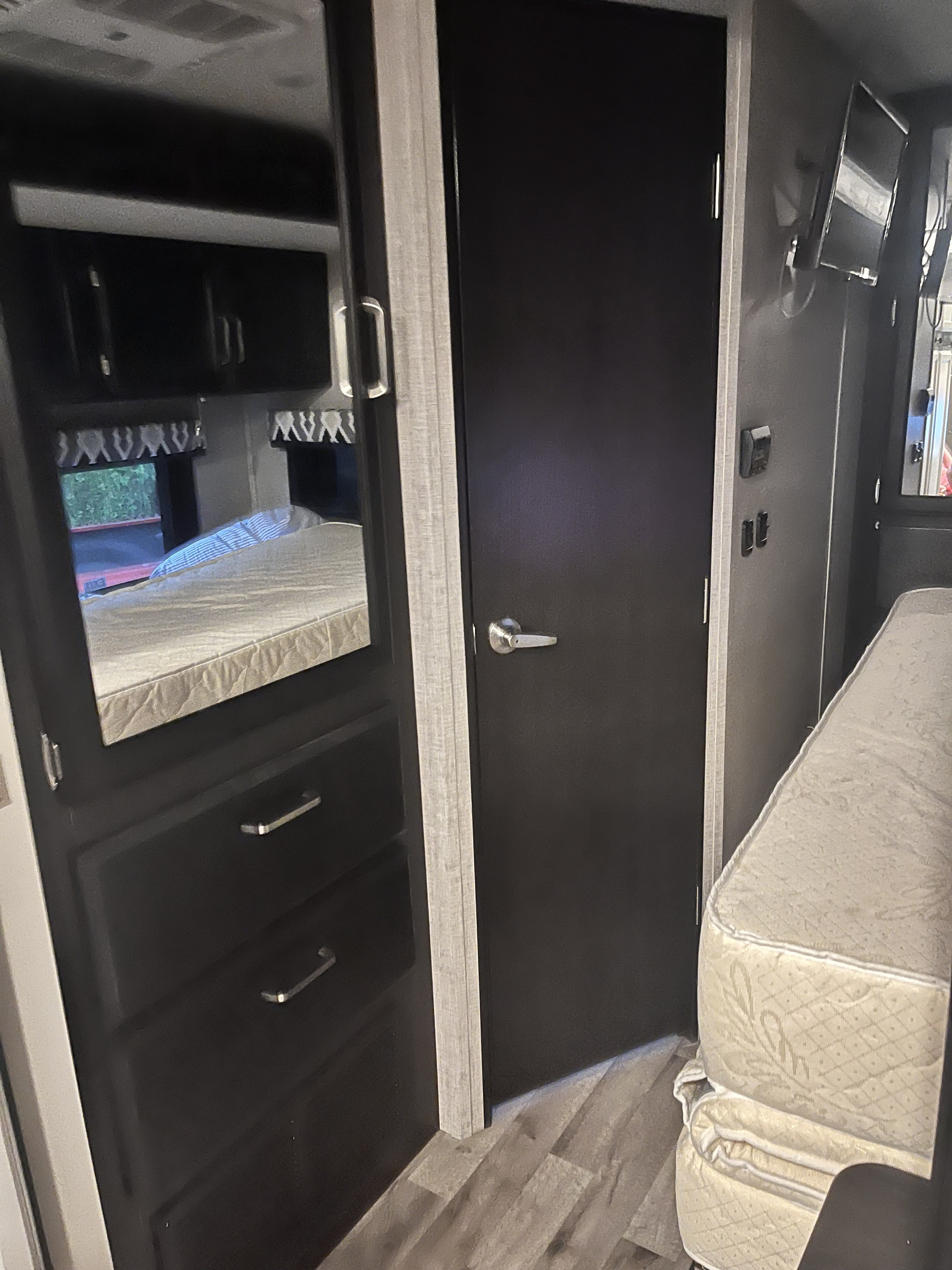 RV rental bedroom interior, featuring a mirrored wardrobe reflecting the bed, a dark door, and a wall-mounted TV.. Jayco Greyhawk 2022