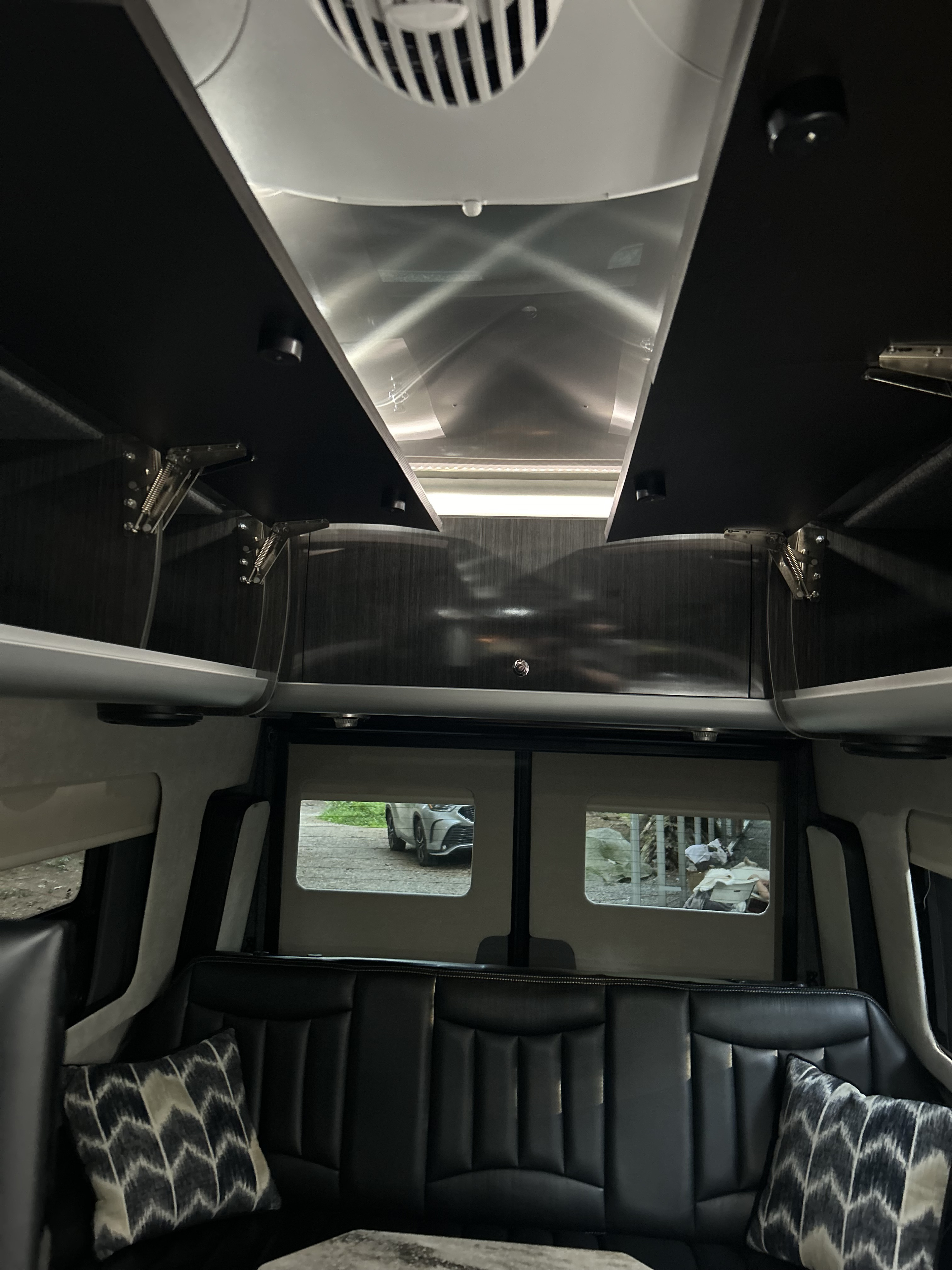 Spacious RV rental interior: plush black leather seating, overhead storage, and a bright, reflective ceiling.. Airstream Interstate 2016