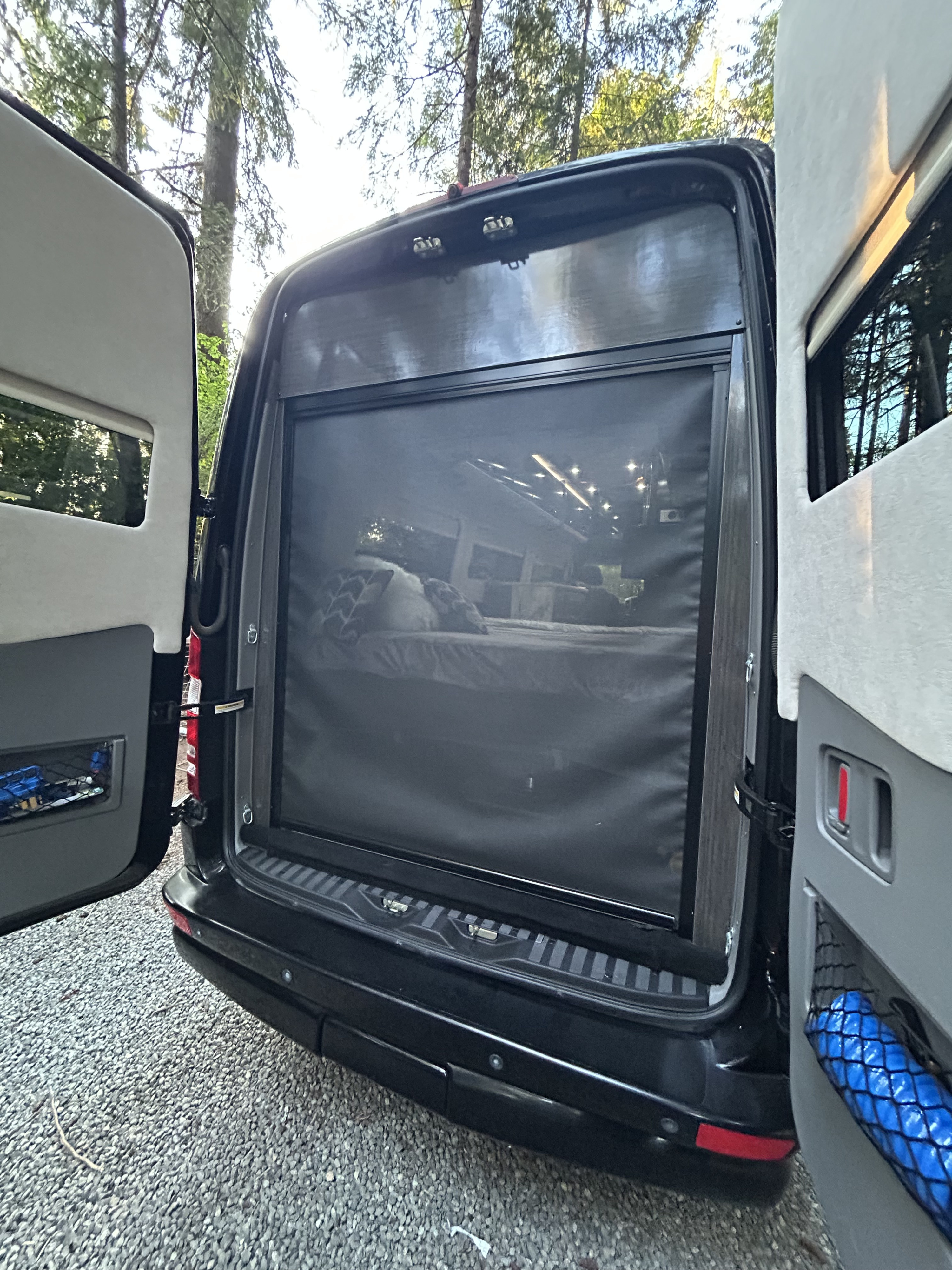 Open back doors of an RV rental revealing a comfortable bed with a mosquito screen, perfect for peaceful camping nights.. Airstream Interstate 2016