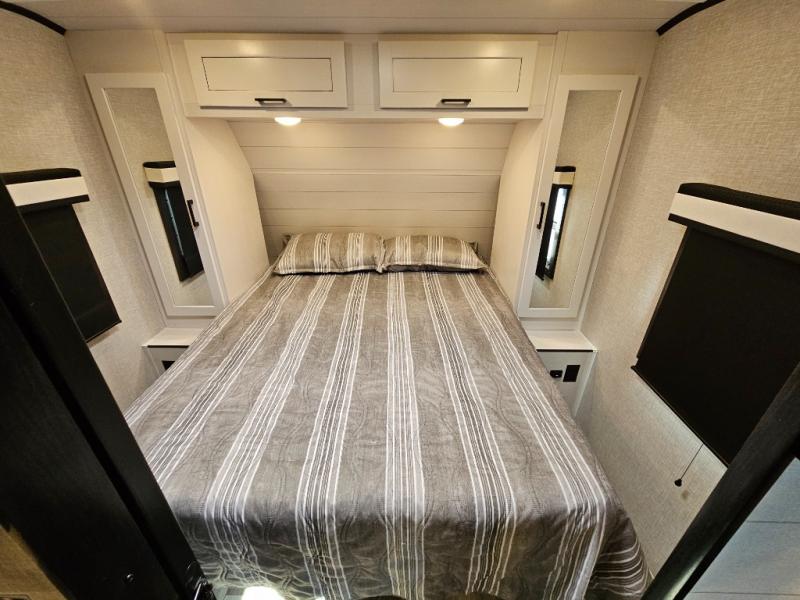 A cozy RV rental bedroom features a queen-sized bed with striped bedding, overhead cabinets, and mirrored wardrobes on each side.. Jayco Jay Feather 2024