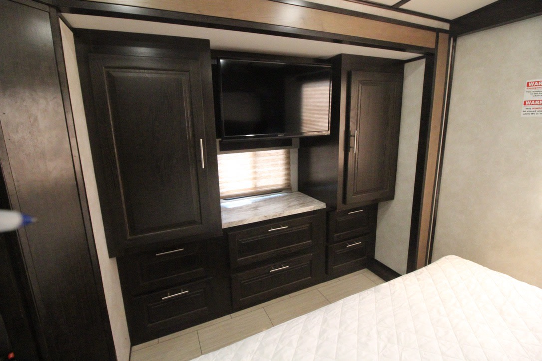 RV rental bedroom with dark wood cabinets, a wall-mounted TV, window, and multiple drawers. Compact and organized interior.. Forest River FR3 2020
