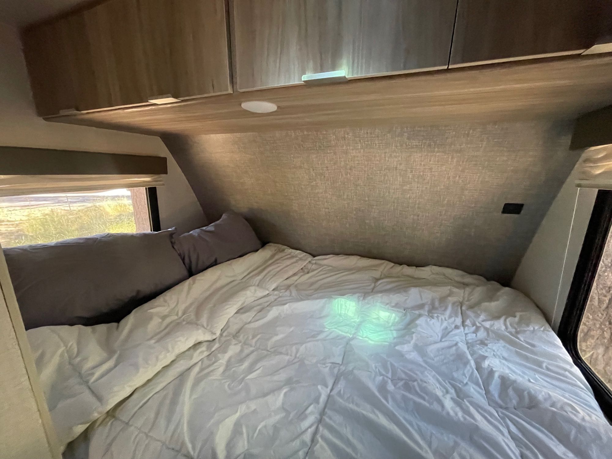 Cozy RV rental bedroom with white comforter, gray pillows, and overhead cabinets.. Winnebago Micro Minnie 2021