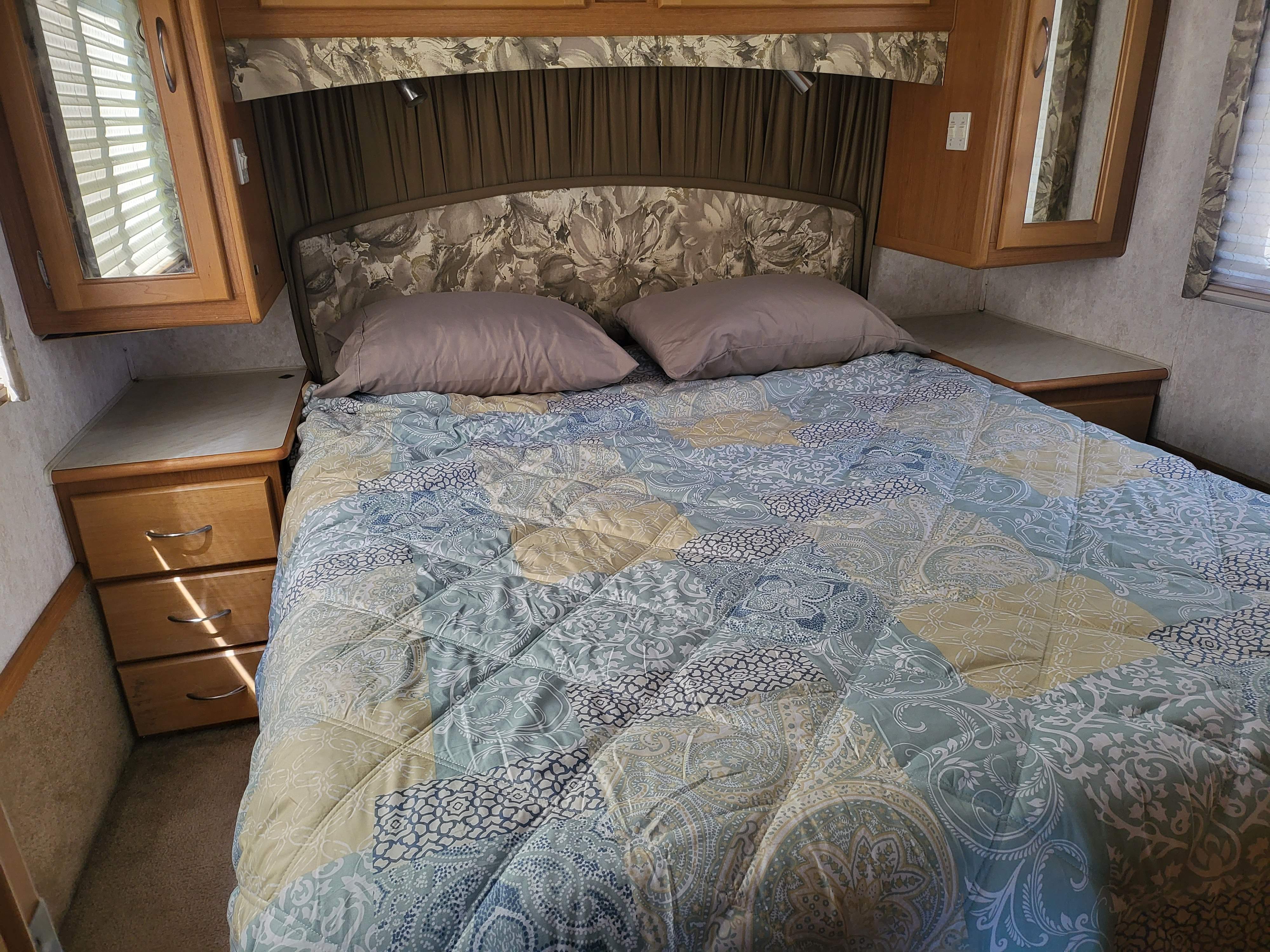 Comfortable RV rental bedroom: plush bed with patterned quilt, wood cabinetry, nightstands, and reading light.. Southwind Southwind Motorhome 2000