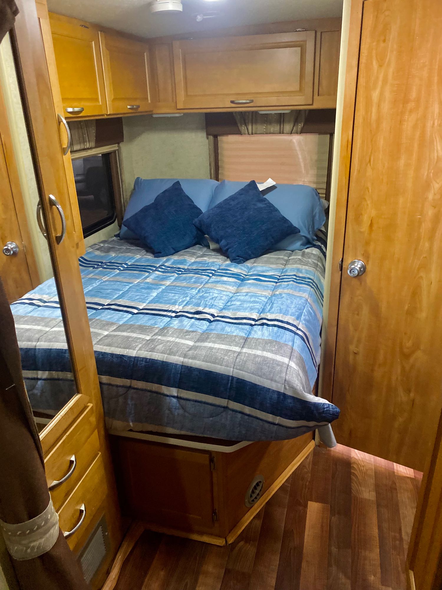 Inside an RV rental: a comfortable bedroom with blue striped bedding, wooden storage, and warm wood floors.. Winnebago Cambria 2008