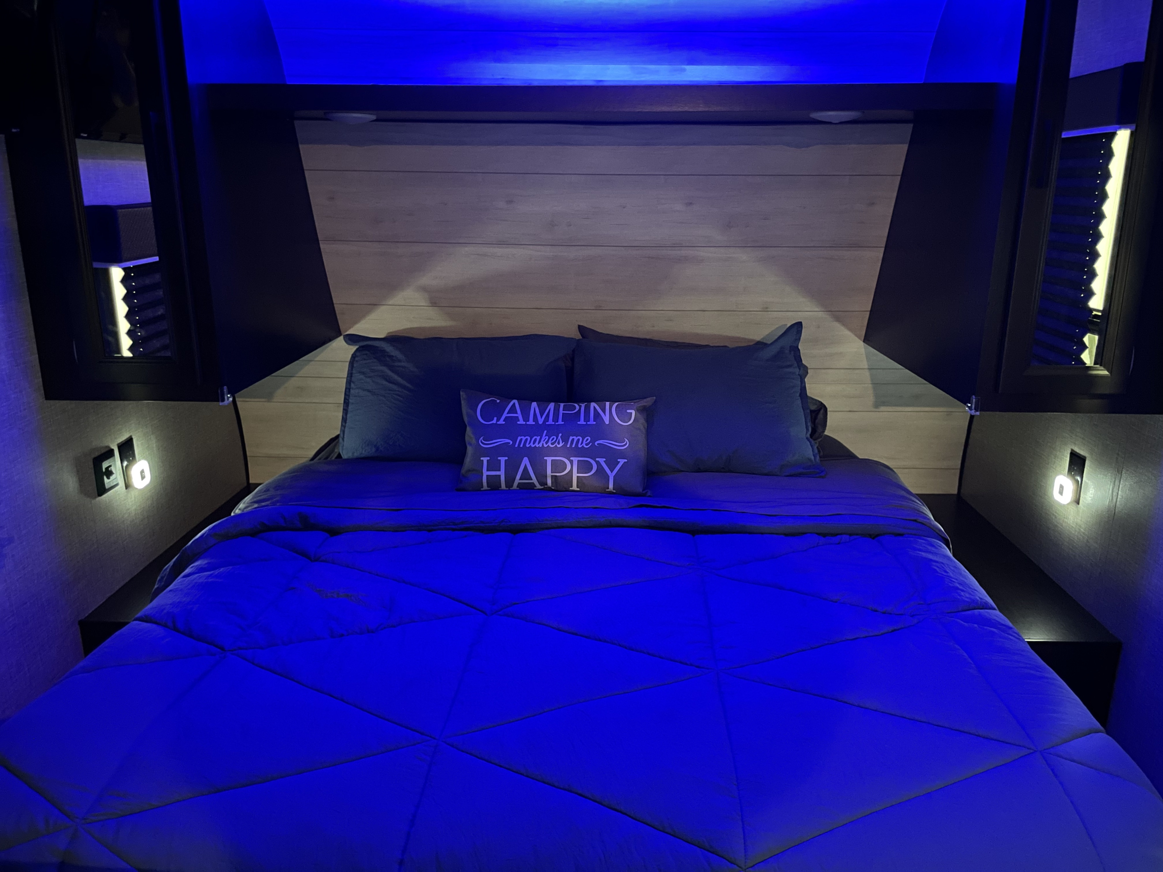 Cozy RV rental bedroom with blue mood lighting, a comfortable bed, and a "Camping makes me HAPPY" pillow.. Jayco Jay Flight SLX 2022