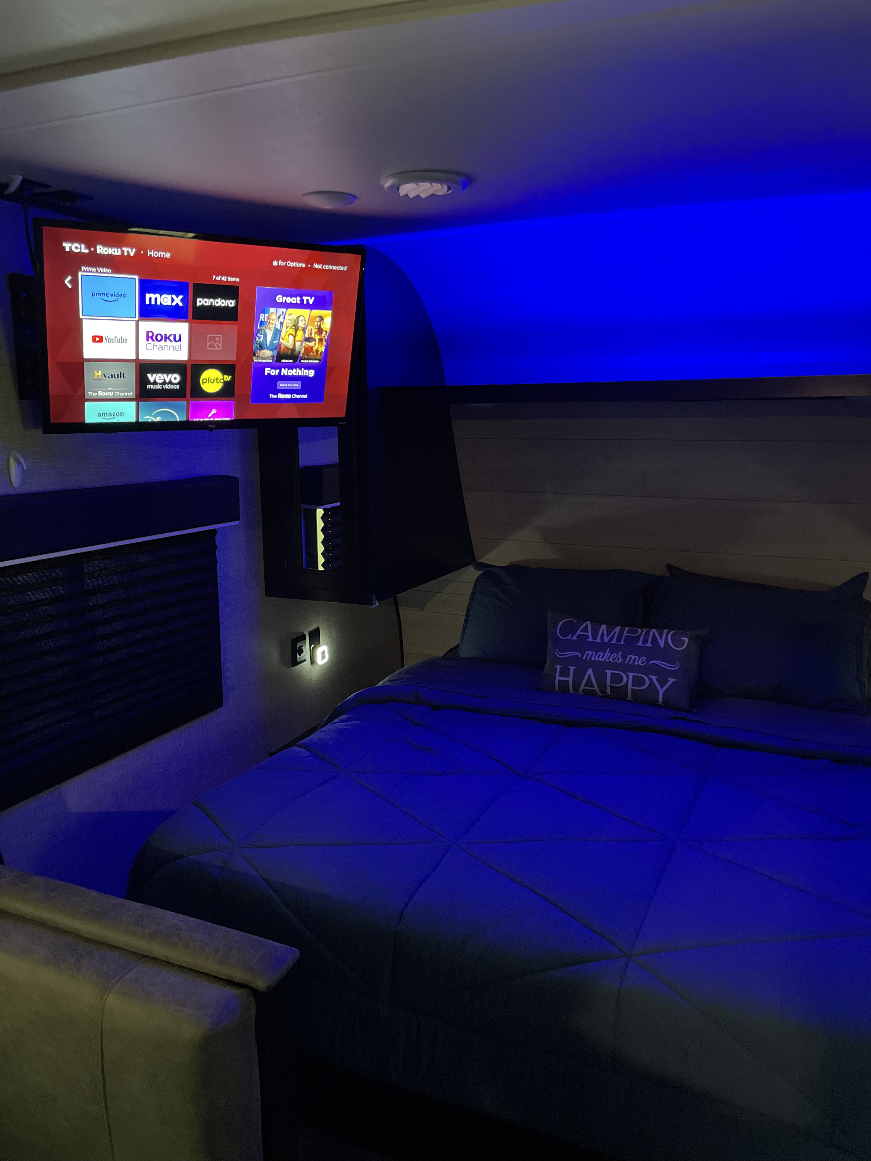 RV rental interior features a snug bedroom with a Roku TV, ambient blue lights, and a cozy "Camping makes me Happy" pillow.. Jayco Jay Flight SLX 2022
