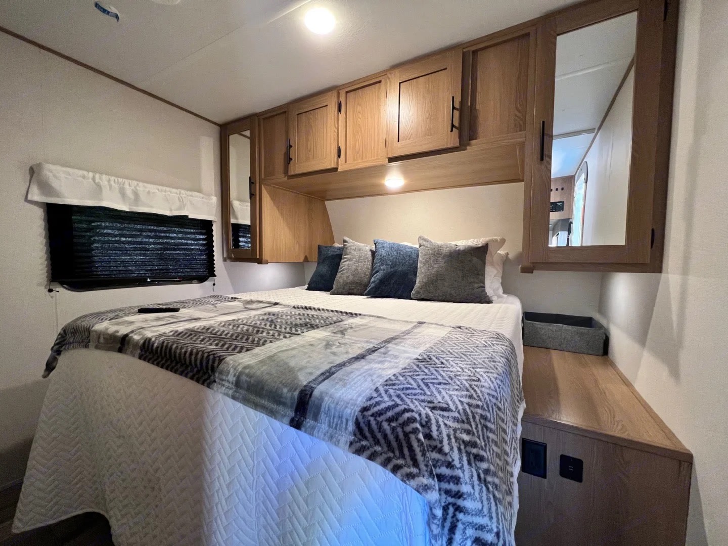 An RV rental bedroom features a comfy bed with a patterned blanket, overhead cabinets, a window, and a bedside counter.. Prime time Avenger 26BK 2023
