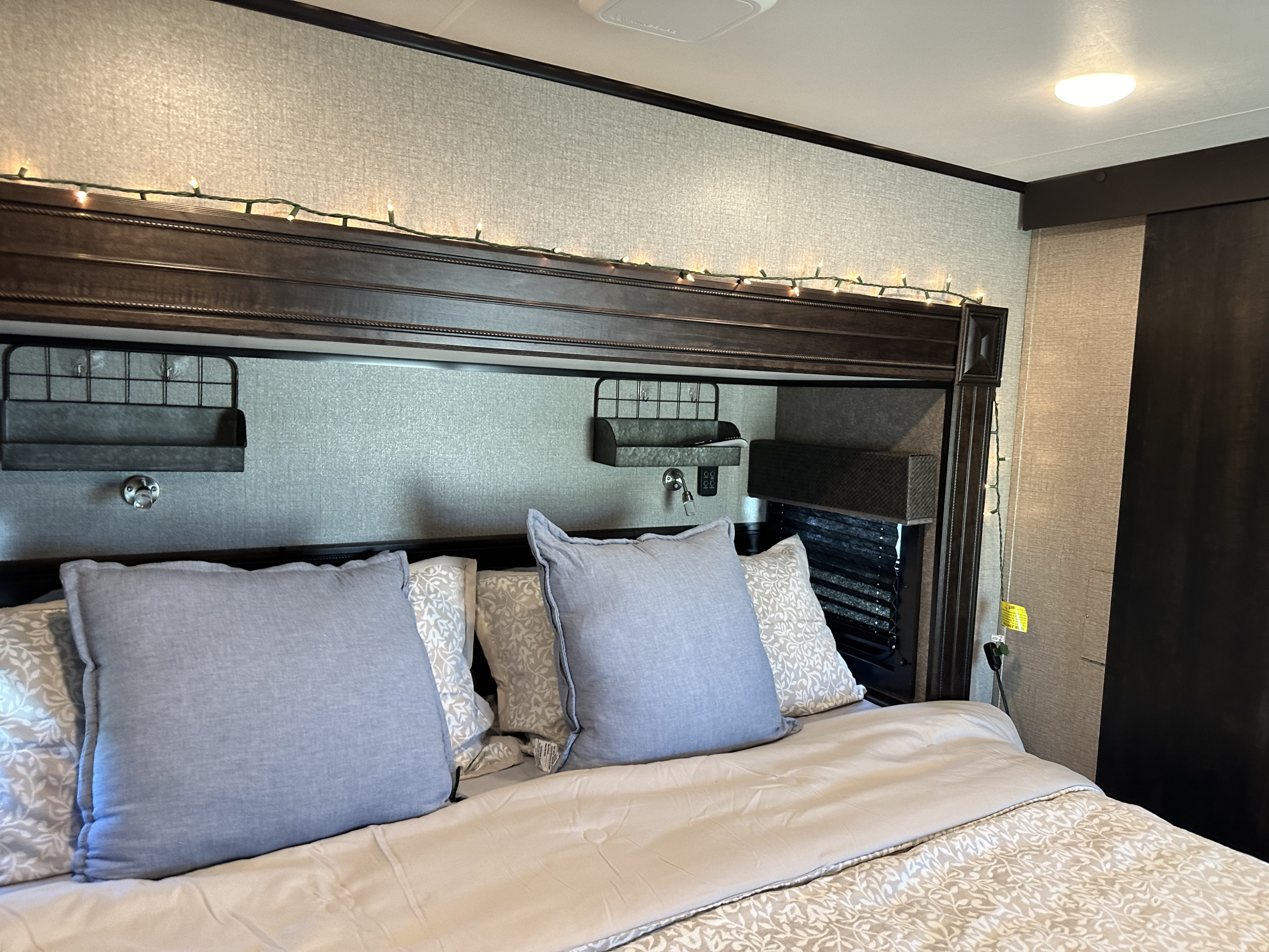 Cozy RV rental bedroom featuring a bed with pillows, string lights, and built-in headboard storage shelves.. Jayco Eagle 2020