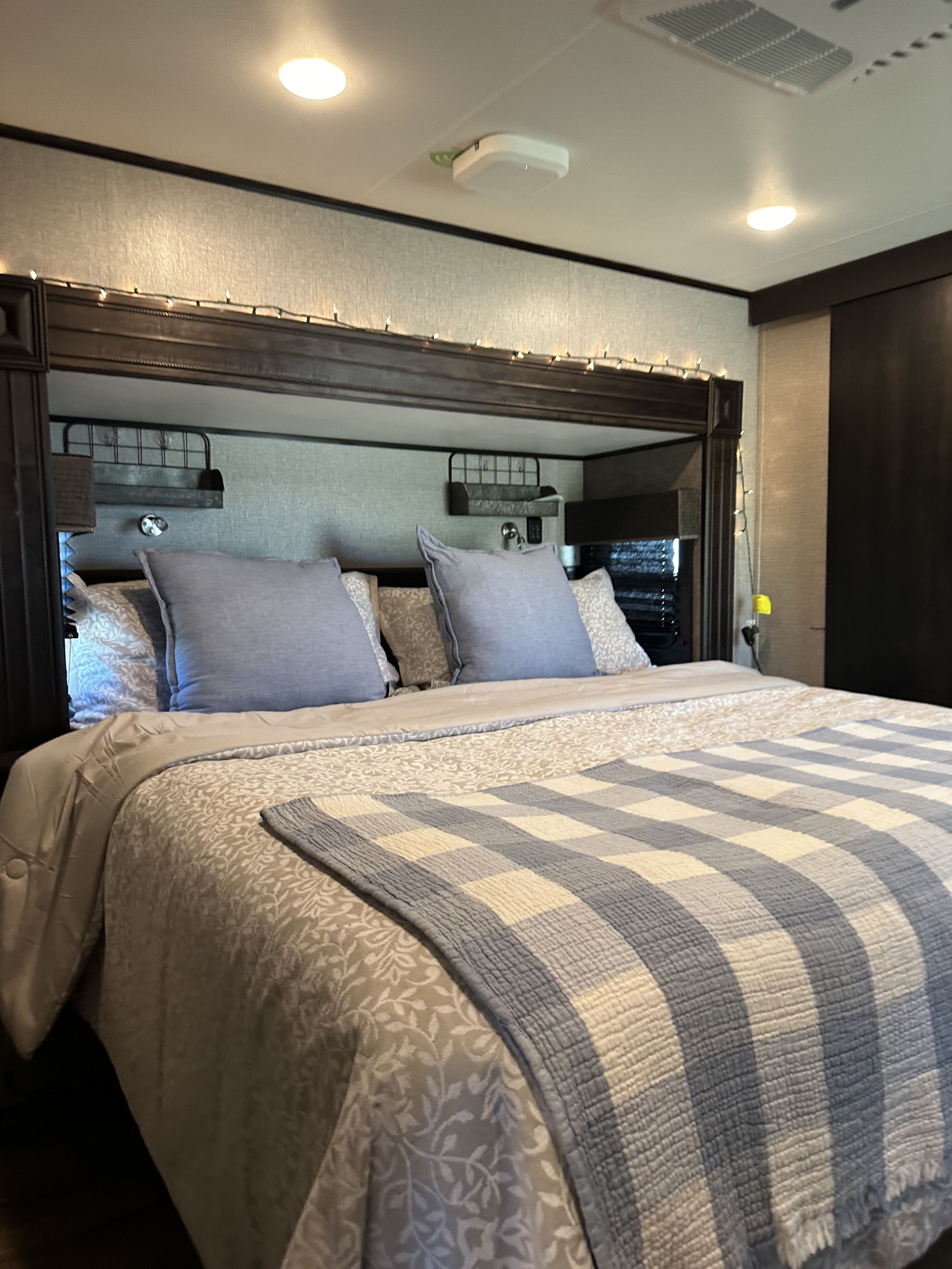 Cozy RV rental bedroom with patterned bedding, a soft blue throw, and string lights for ambiance. AC vent visible.. Jayco Eagle 2020