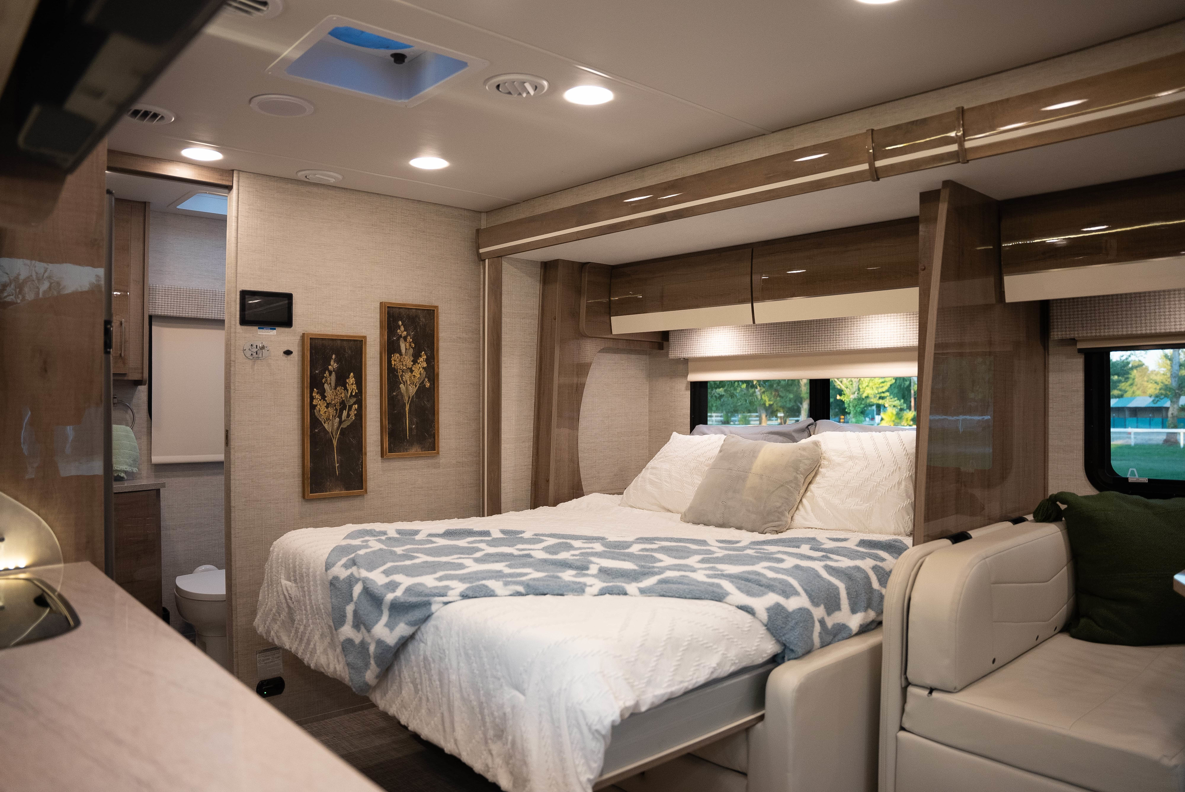 Modern RV rental interior with a comfortable bedroom, overhead cabinets, and cozy seating. Features a light color scheme.. Entegra Coach Other 2023