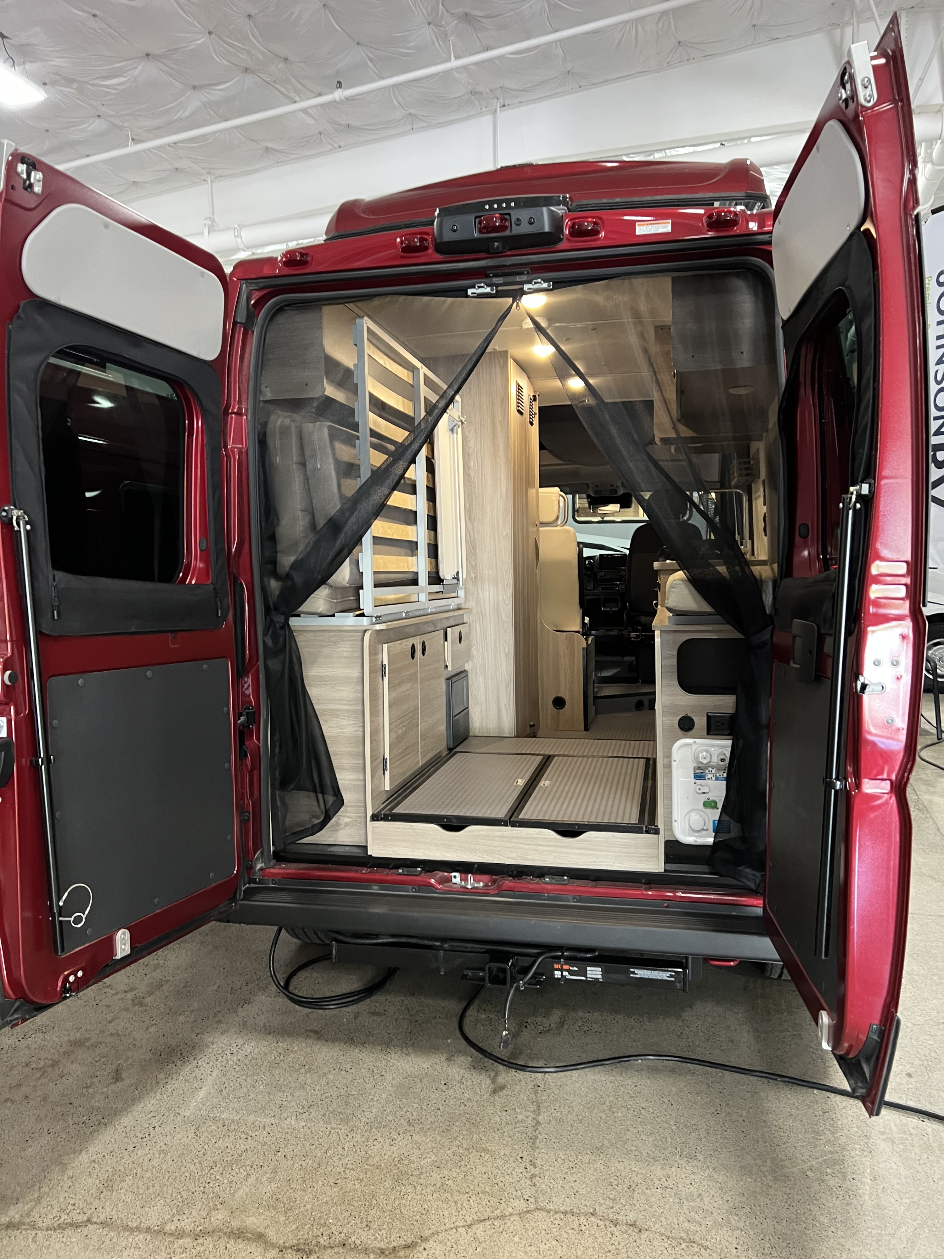 Experience adventure with this RV rental! Rear view of a red camper van interior, showcasing compact living space, cabinetry, and a mosquito net.. Winnebago Solis 2023