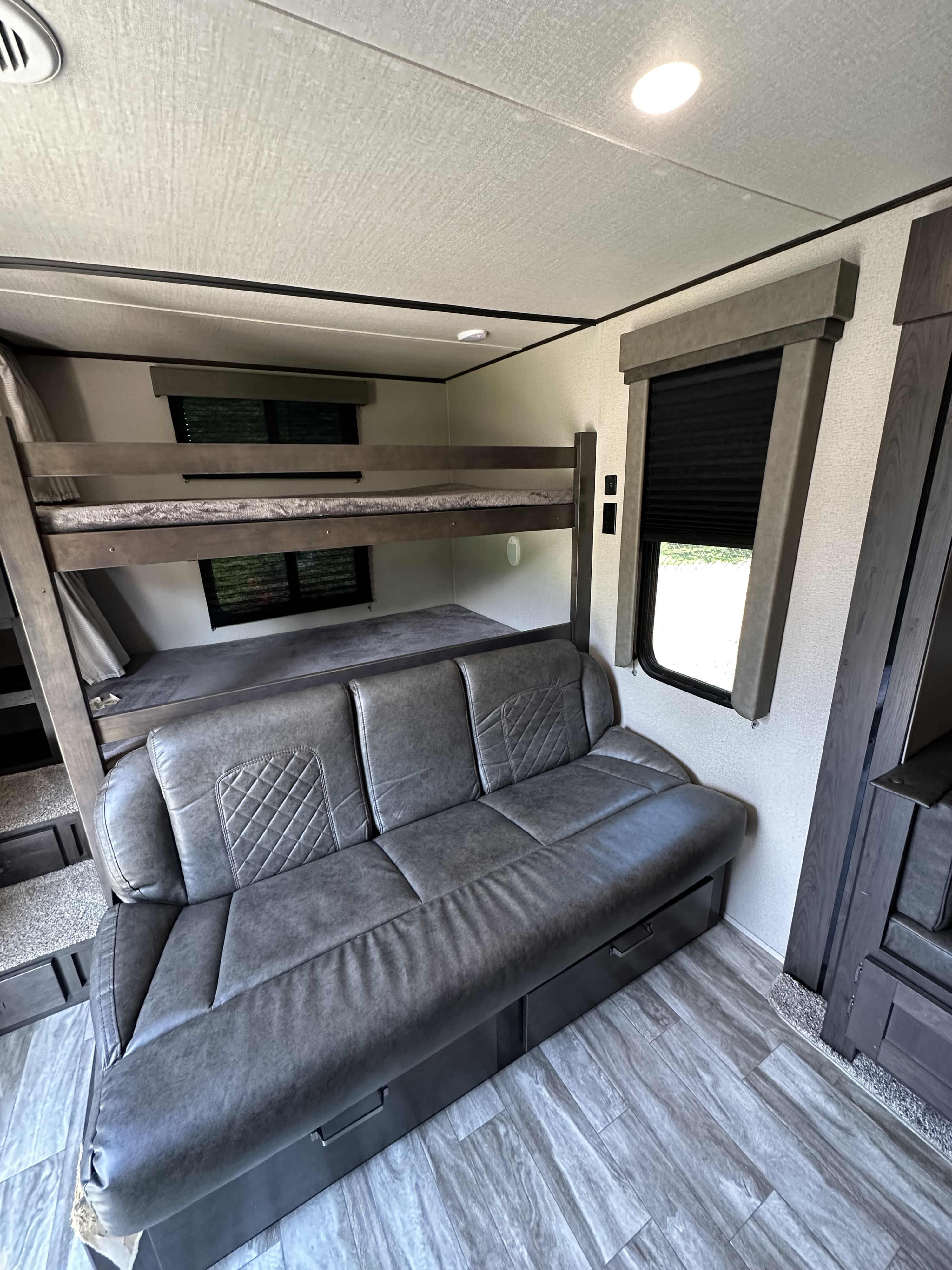 RV rental interior: spacious living area with comfortable grey sofa, convenient storage, and sturdy bunk beds.. Grand Design Transcend Xplor 2021